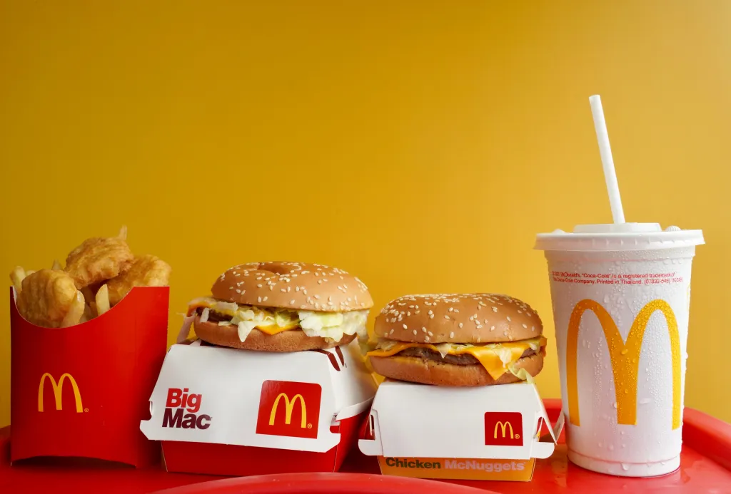 A McDonald's Big Mac, cheeseburger, Chicken McNuggets, fries, and a cold drink on a red tray with a yellow background.