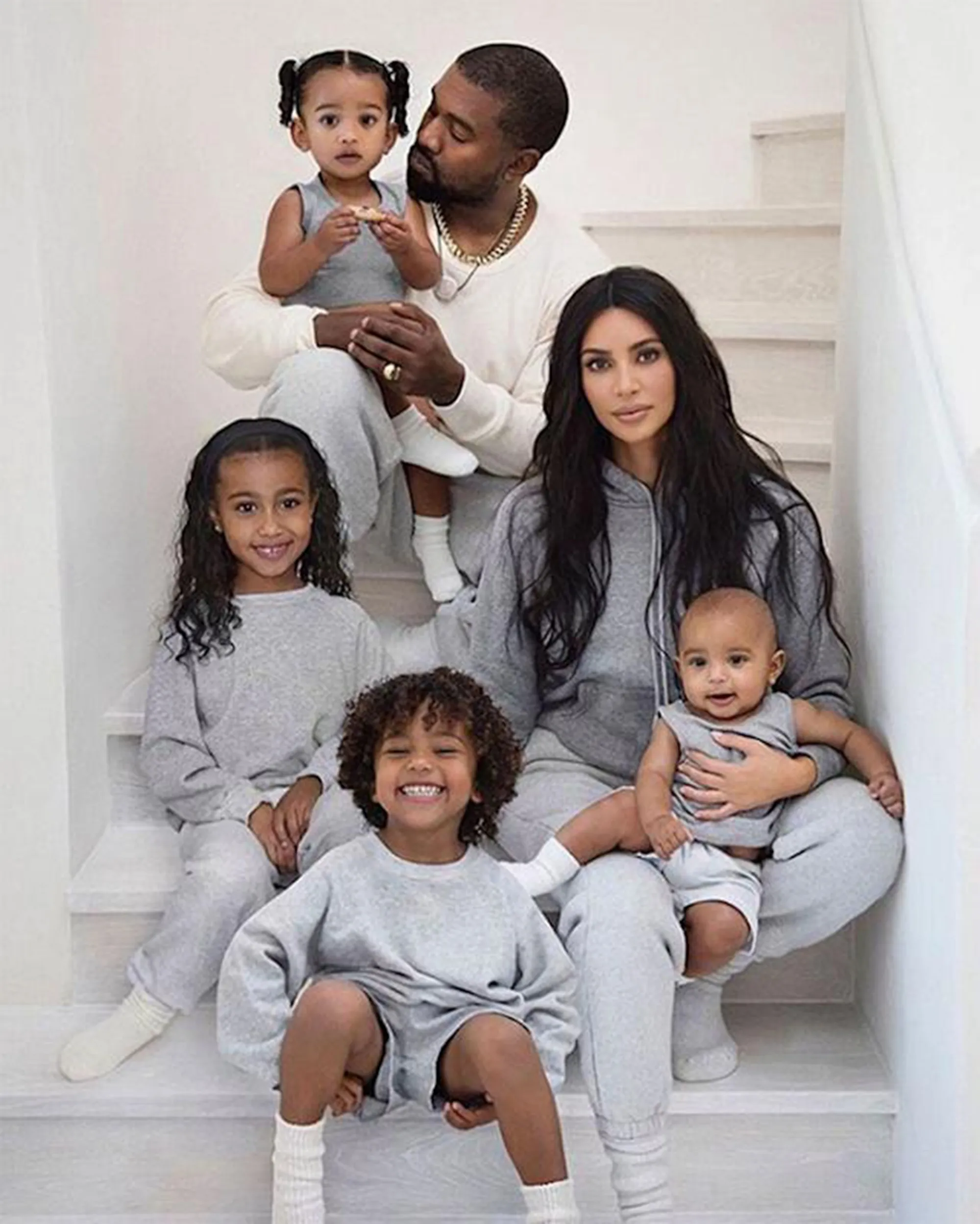 Kanye West and Kim Kardashian pose with their four children, all wearing gray, on a white staircase.
