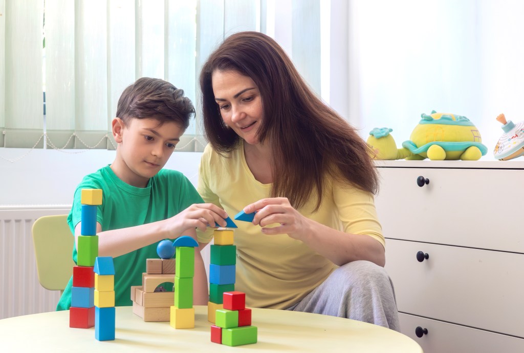 A young boy and woman playing with colorful wooden blocks at home.