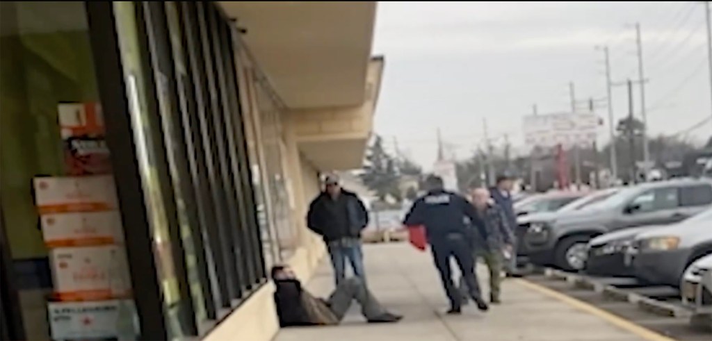 A man is tackled by a police officer on a sidewalk outside of a store.
