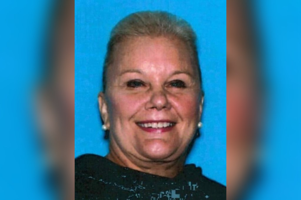 Mugshot of a smiling woman with light hair in a black top against a blue background.