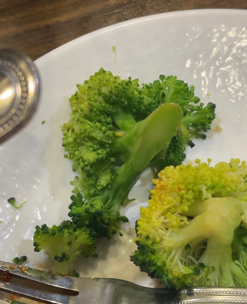 Broccoli florets on a white plate with a fork and spoon.