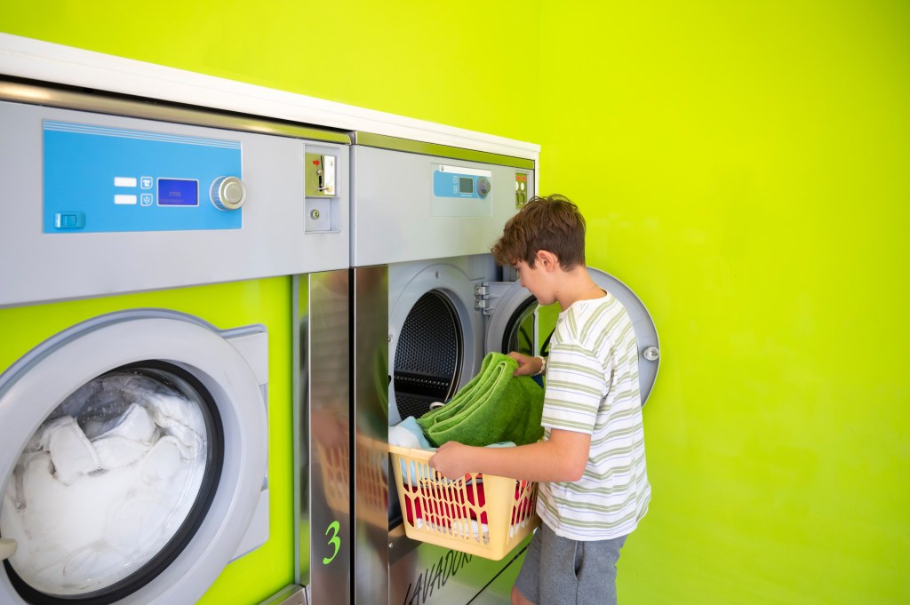 A male teenager loads clothes into a washing machine at a laundromat.