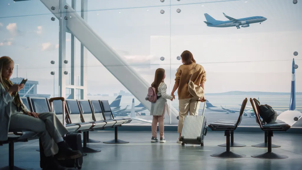 Mother and daughter watching airplanes from an airport terminal window.