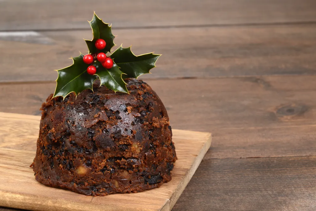 Christmas pudding with holly and berries on a wooden cutting board.
