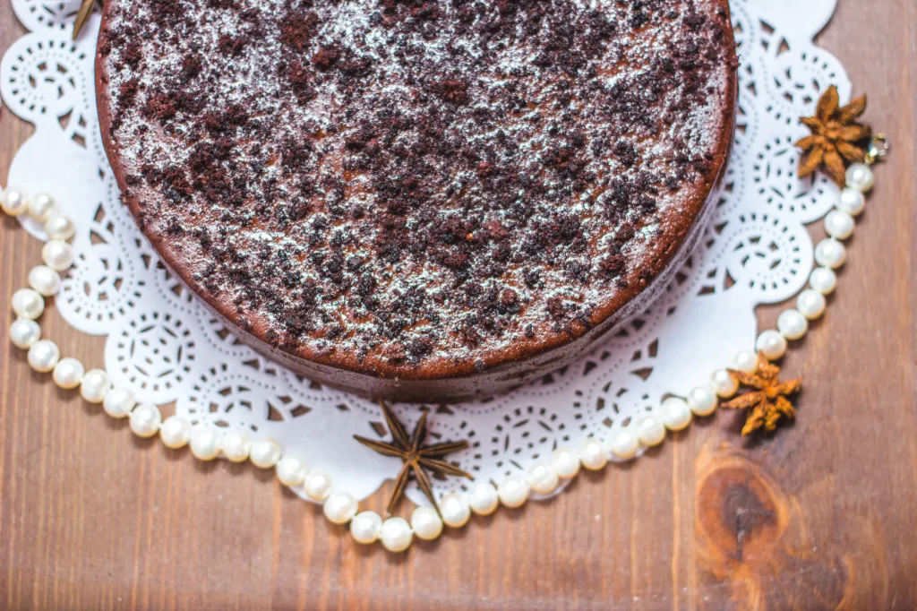 Chocolate cake with powdered sugar and chocolate crumbs on a white doily with a string of pearls and star anise.