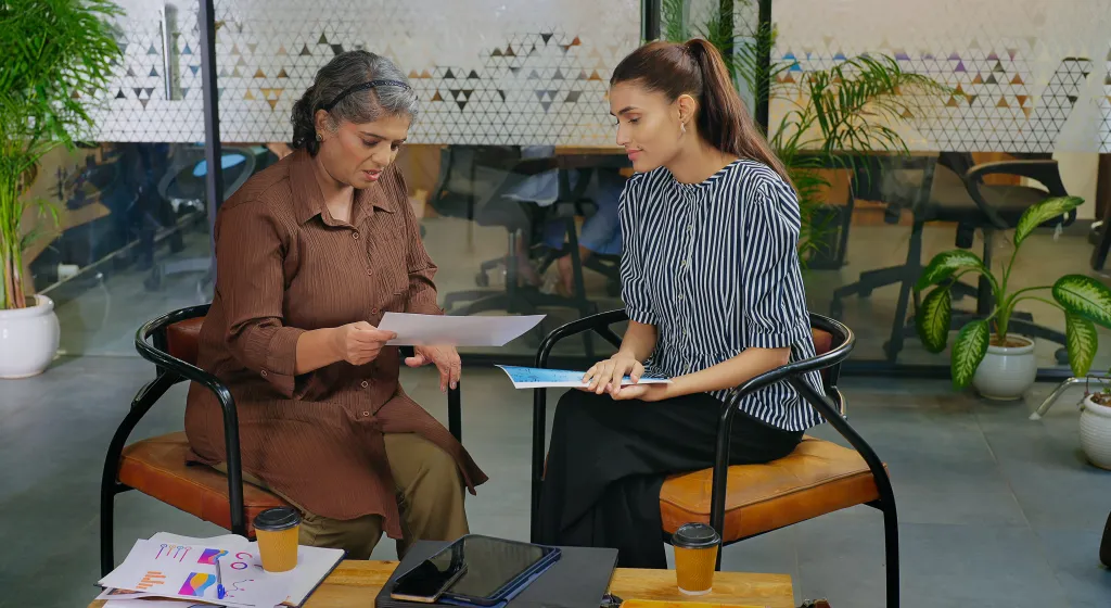 Two businesswomen discussing paperwork in an office setting.