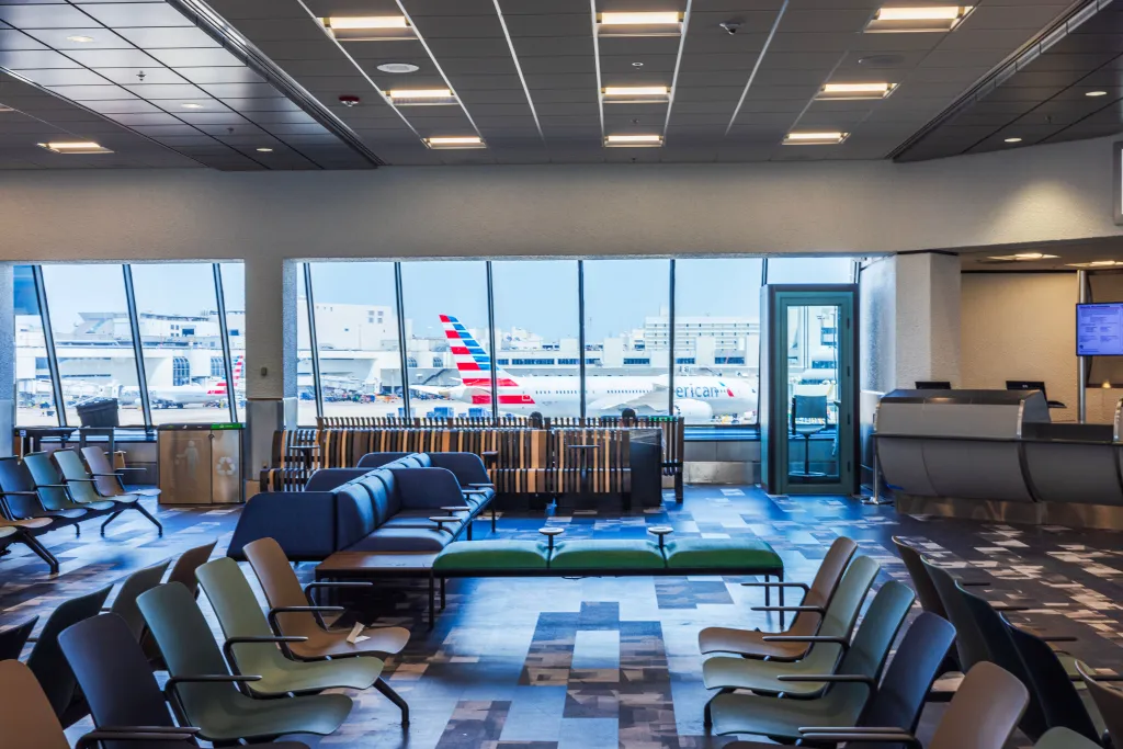 Empty airport gate waiting area with chairs and an American Airlines plane visible on the background in Miami, USA.