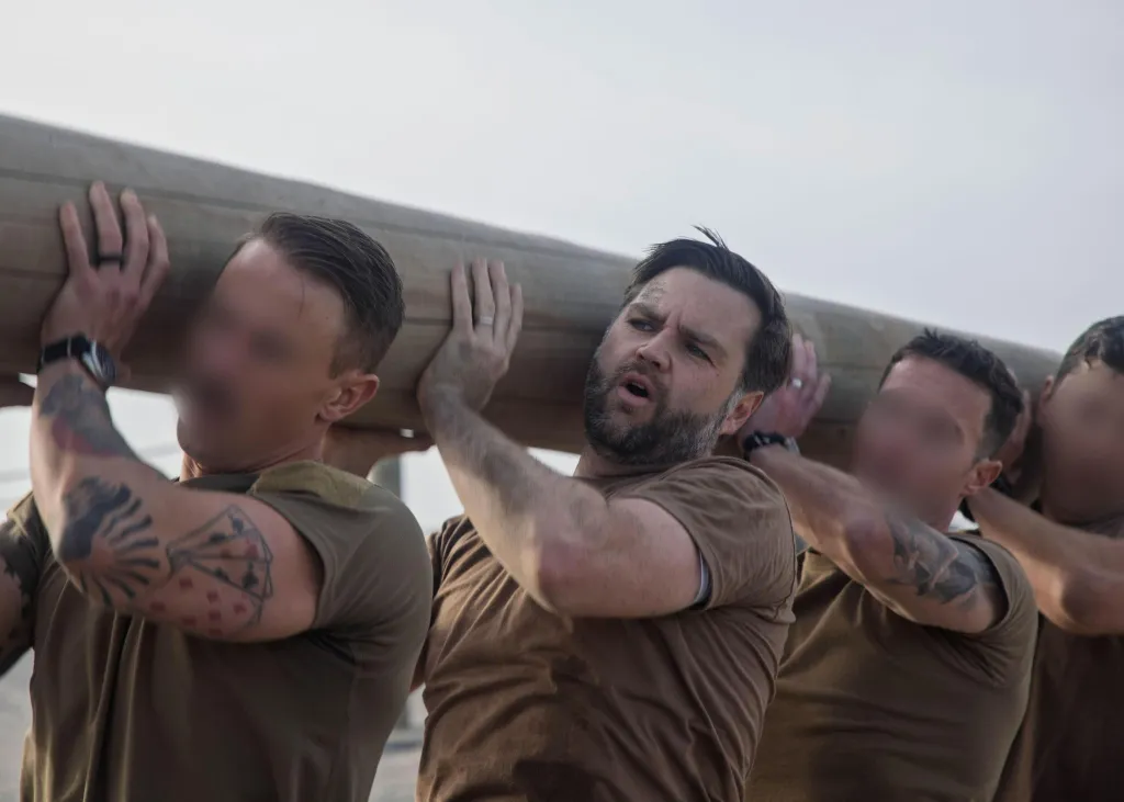 Four men in brown t-shirts carry a large wooden beam on their shoulders.