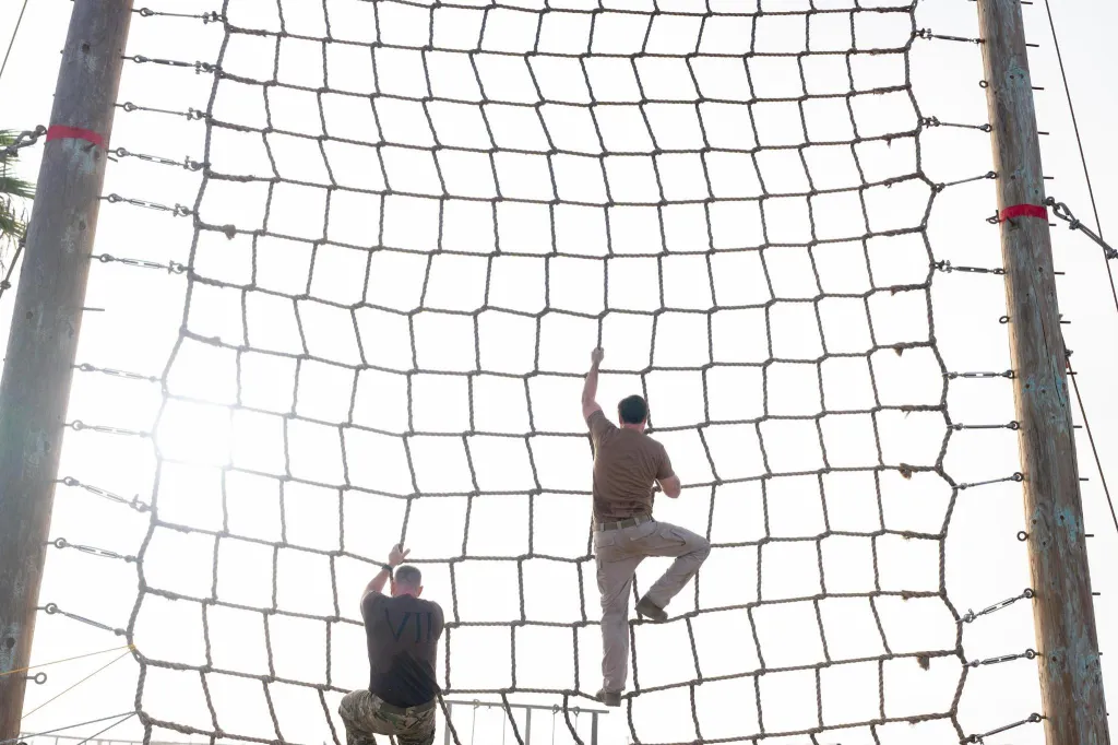 JD Vance and another man climbing a rope net obstacle.