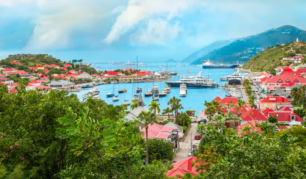 Panoramic landscape of Gustavia harbor in Saint Barthélemy with boats, yachts, and buildings with red roofs.