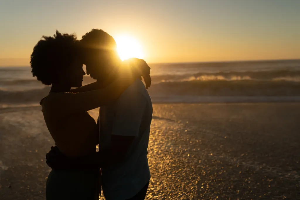 Silhouetted African American couple embracing on a beach at sunset.