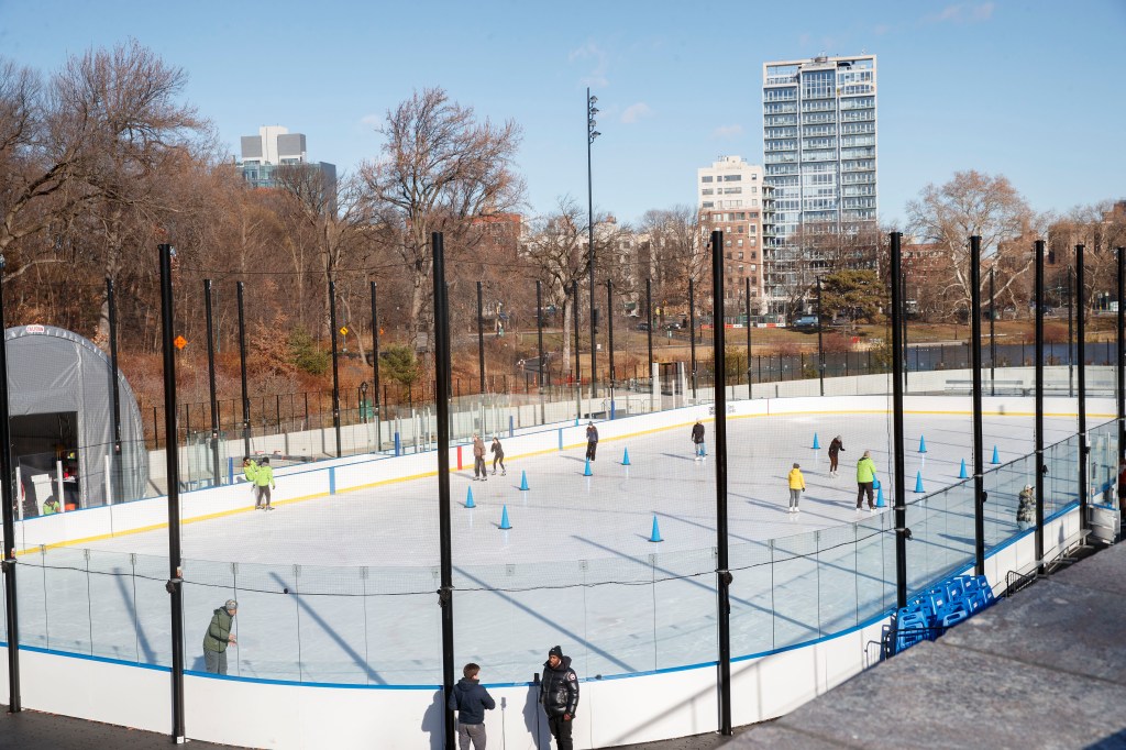 Ice skaters at Gottesman Rink in Central Park, surrounded by trees and tall buildings.