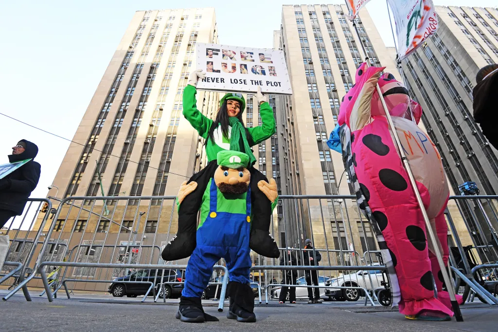 A woman dressed as Luigi from Mario Bros. holds a sign that says