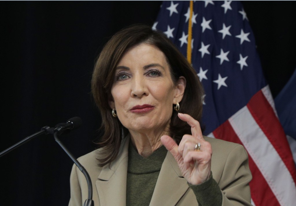 New York Governor Kathy Hochul speaking at a podium with an American flag in the background.