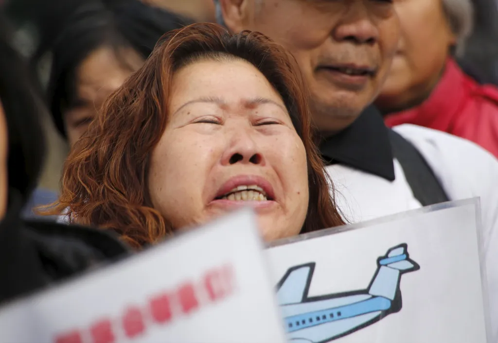 A crying woman holds a sign with an illustration of an airplane.