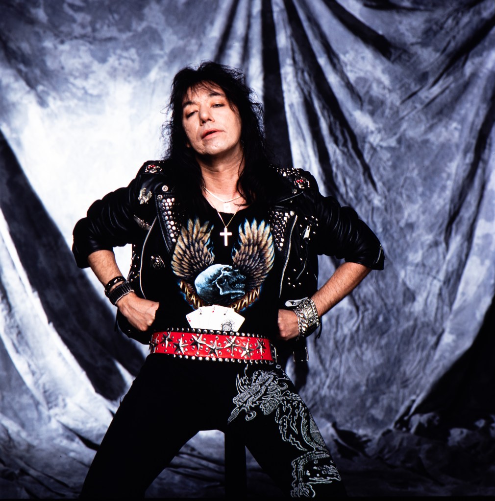 Ace Frehley posing in a studded leather jacket and skull t-shirt.