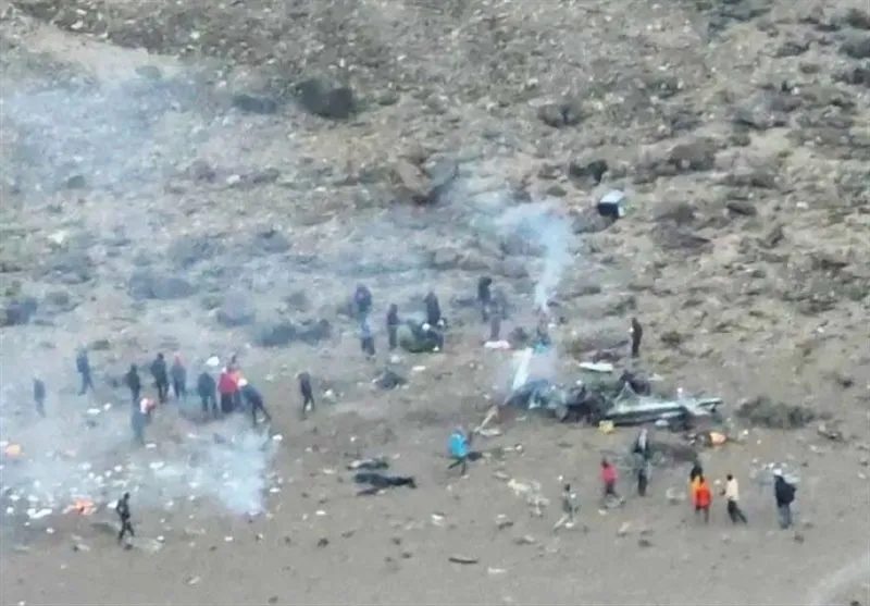 People investigating a plane wreckage on rocky terrain with smoke rising.