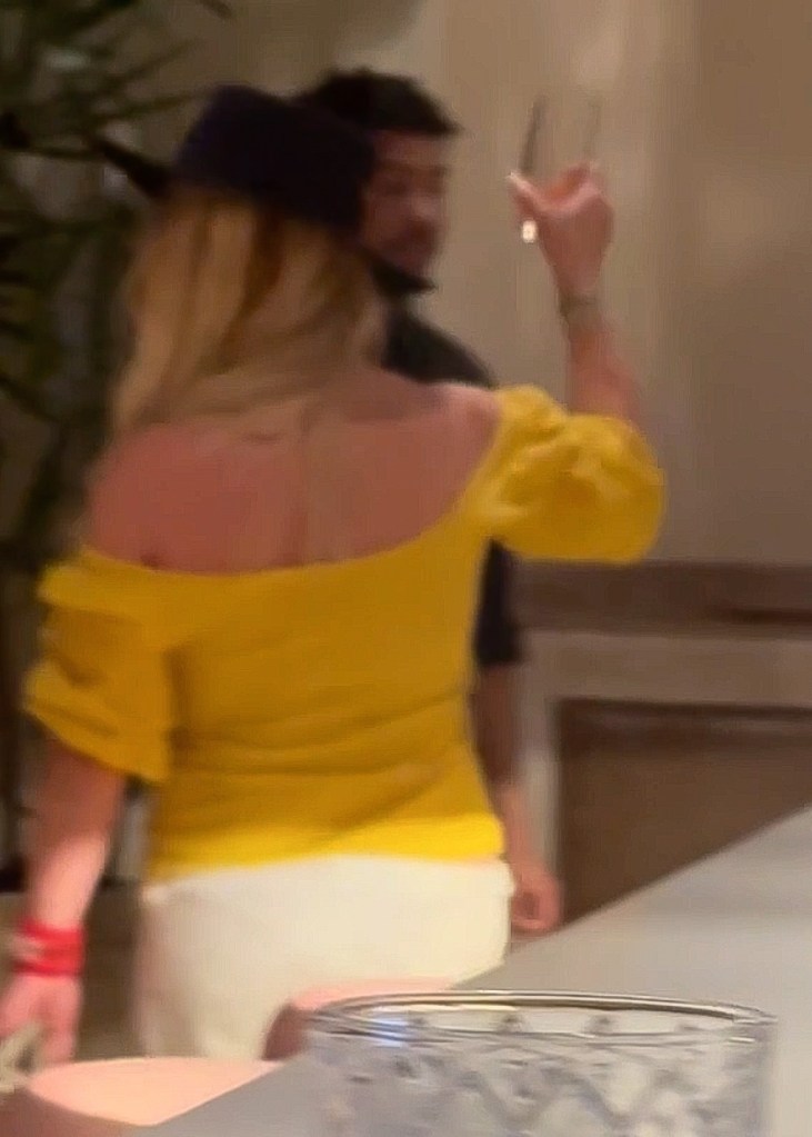 Britney Spears in a yellow off-the-shoulder top, holding a drink and appearing unsteady.
