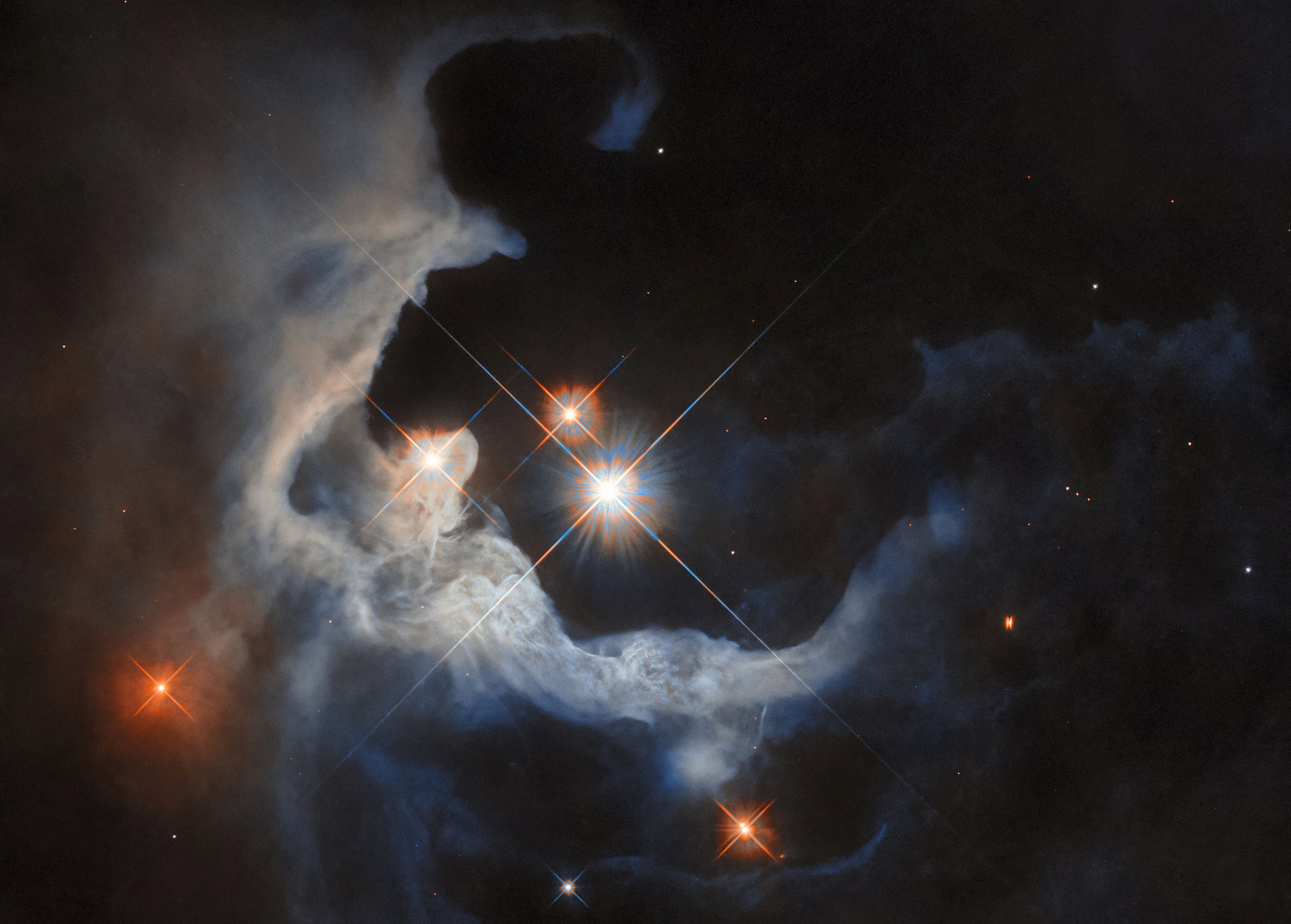 Several bright stars appear surrounded by a large swirling cloud of dust, illuminated by the light of the stars.