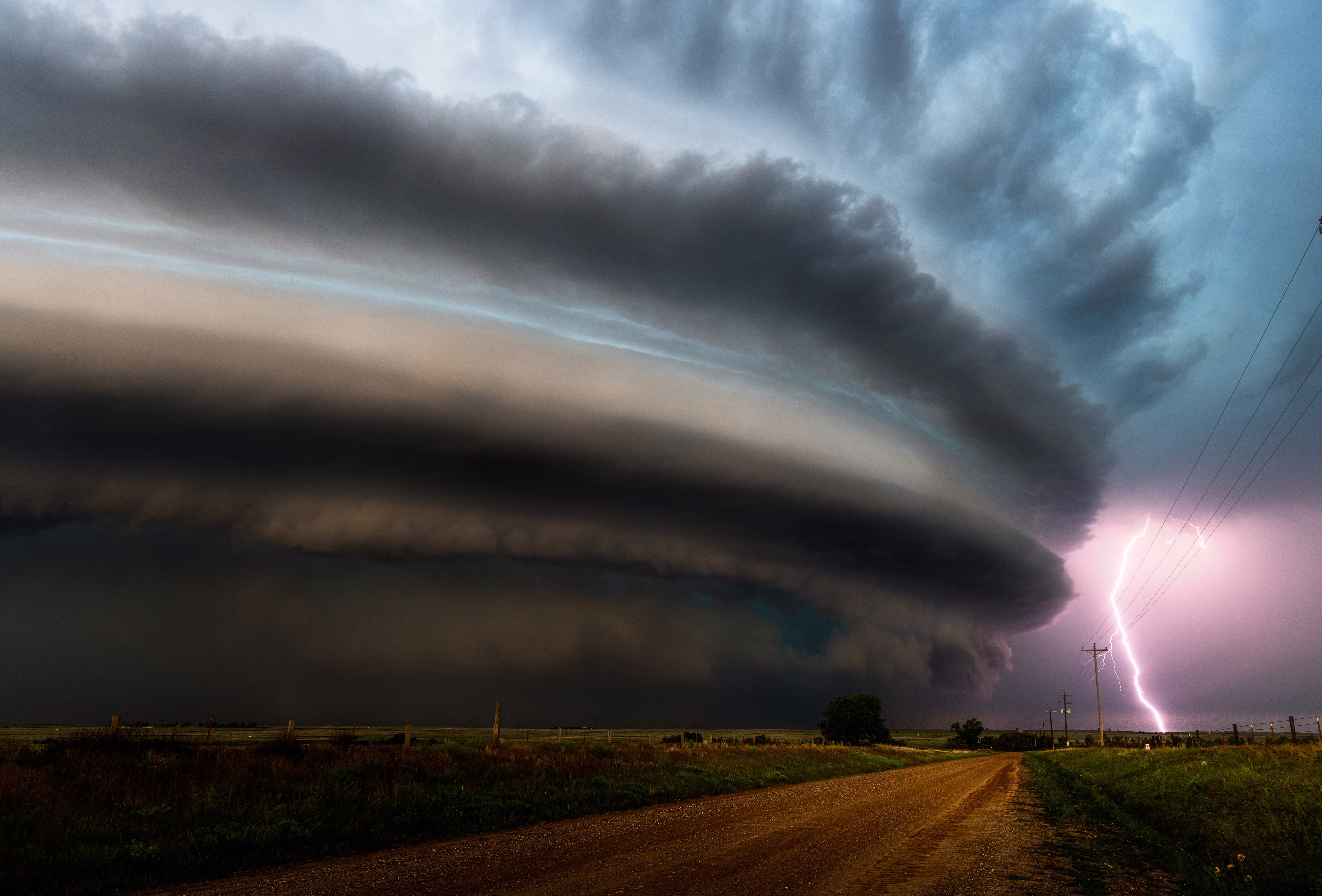 A huge, dark, cylindrical storm cloud swirls above a rural area.