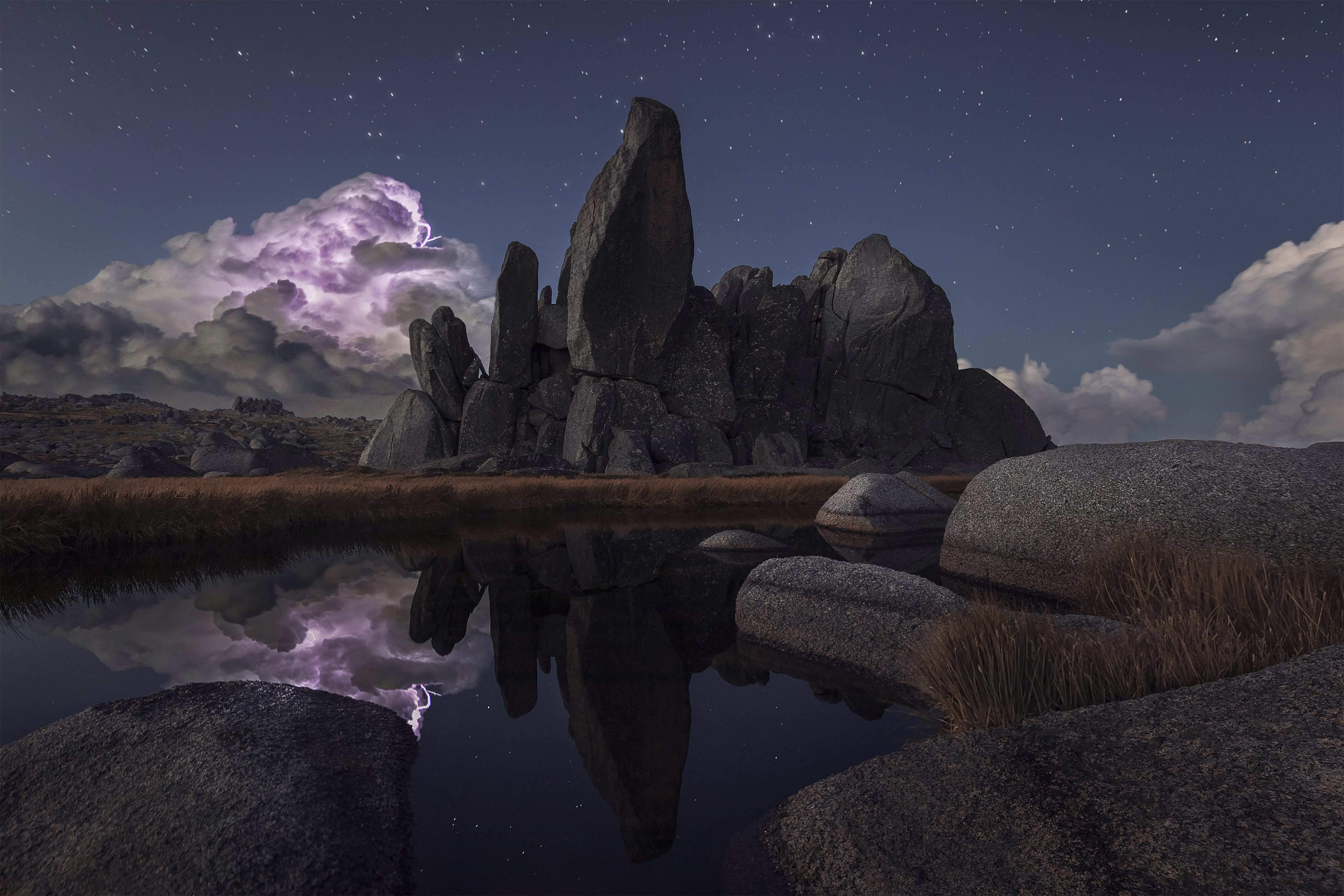 Lightning illuminates a storm cloud behind a large rock formation.