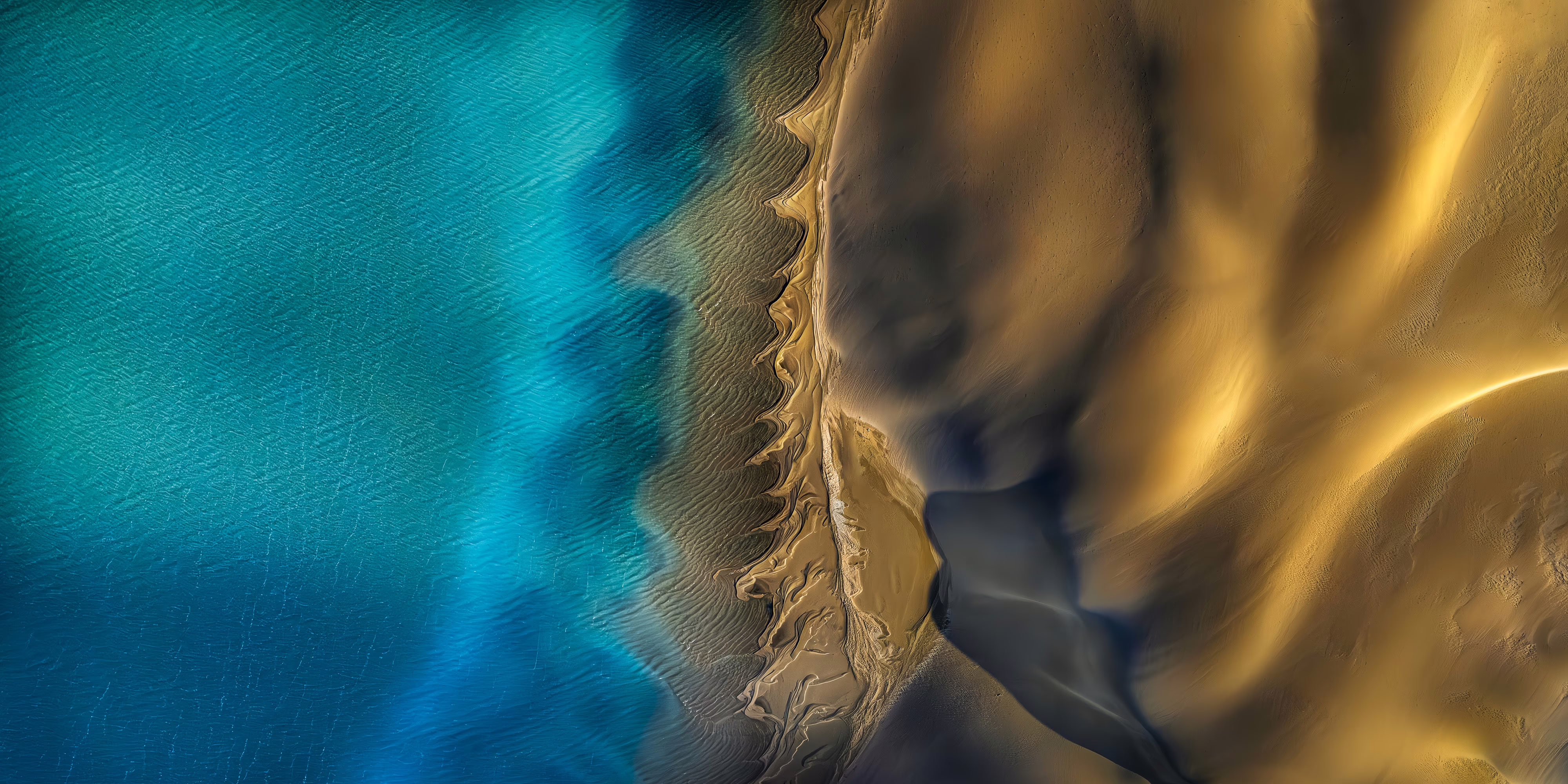 A drone's-eye-view of a sandy coastline beside a blue-green bay.