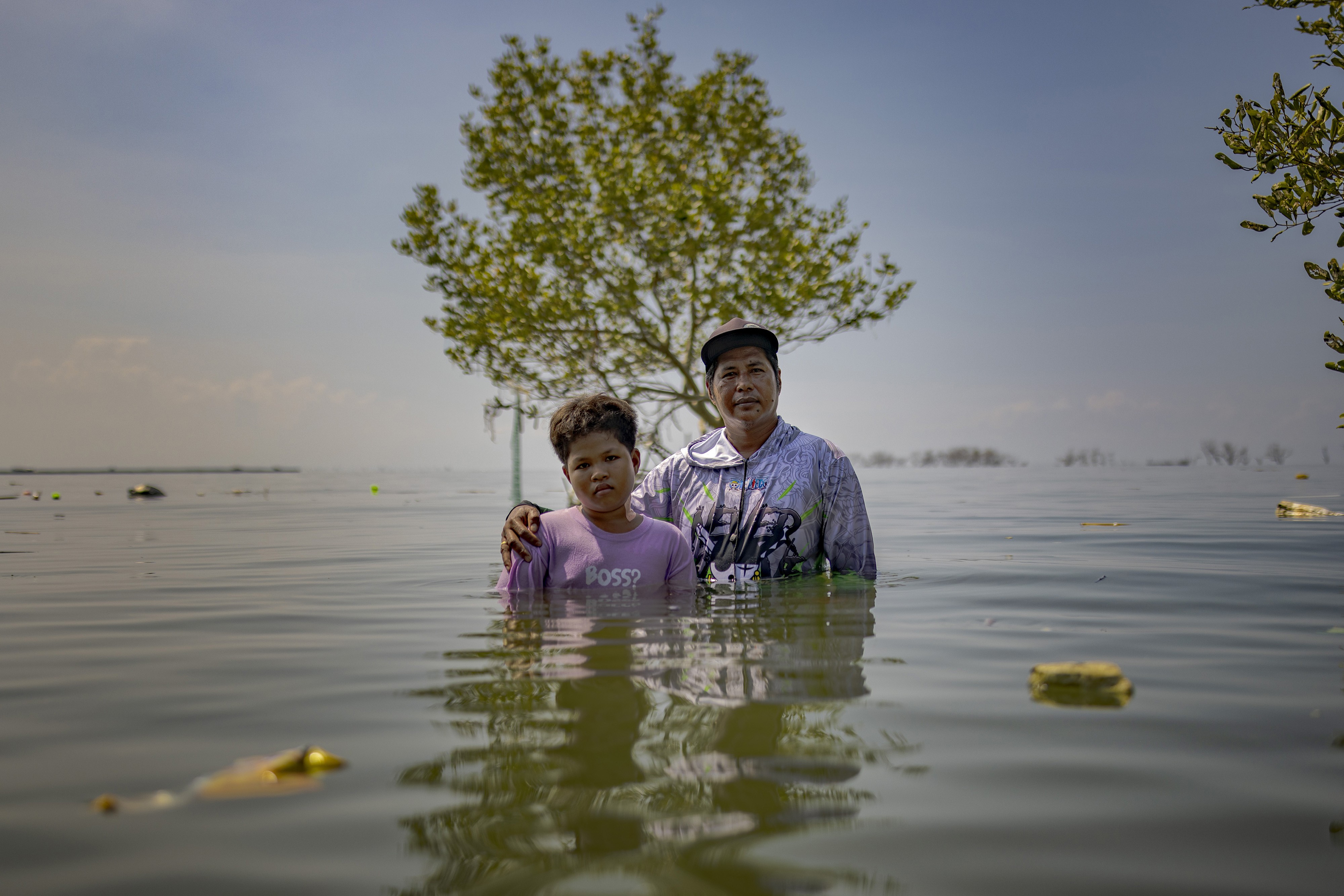 A man and a boy stand side-by-side in chest-deep floodwater.