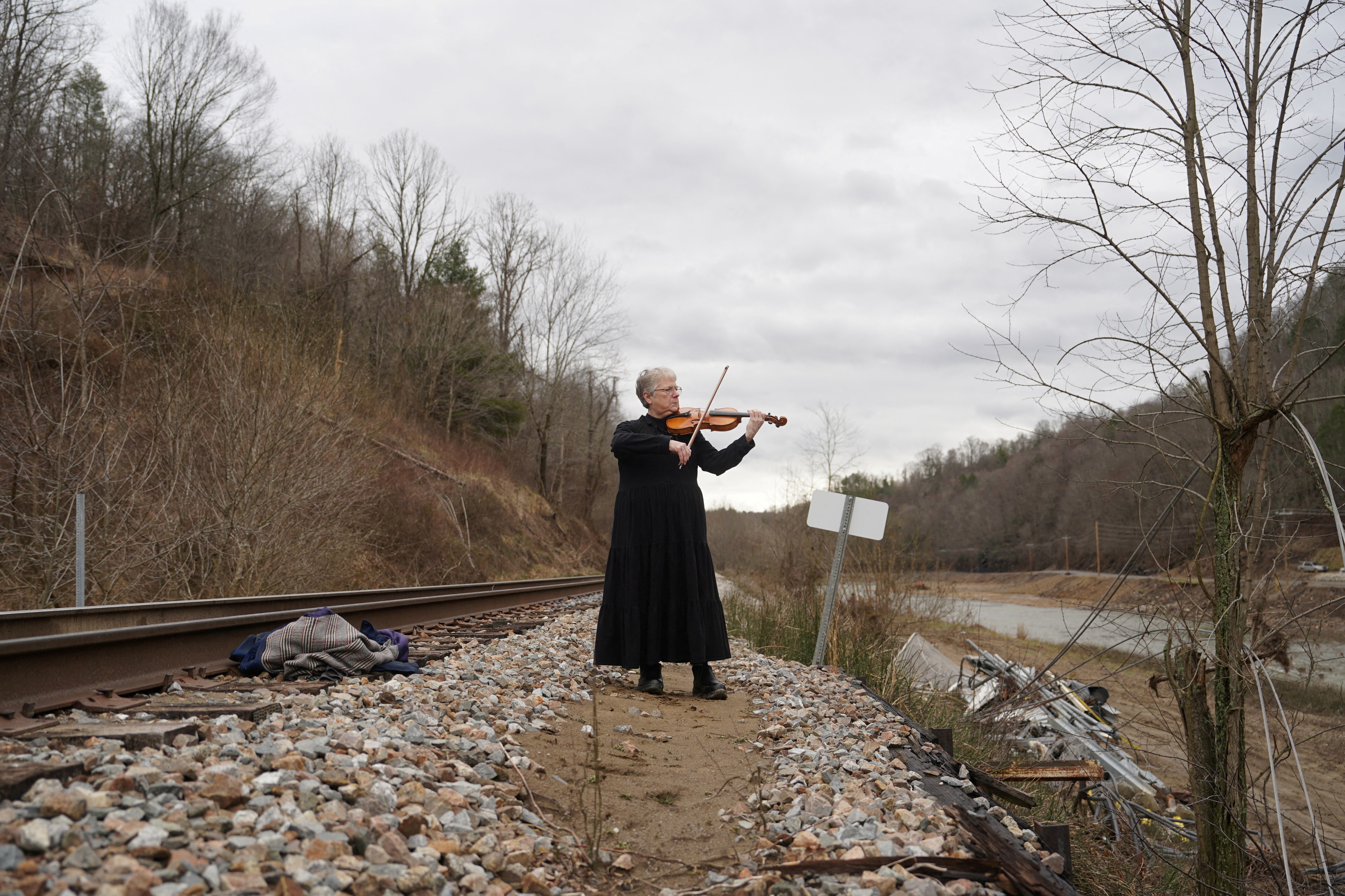 A person stands beside railroad tracks, playing a fiddle.