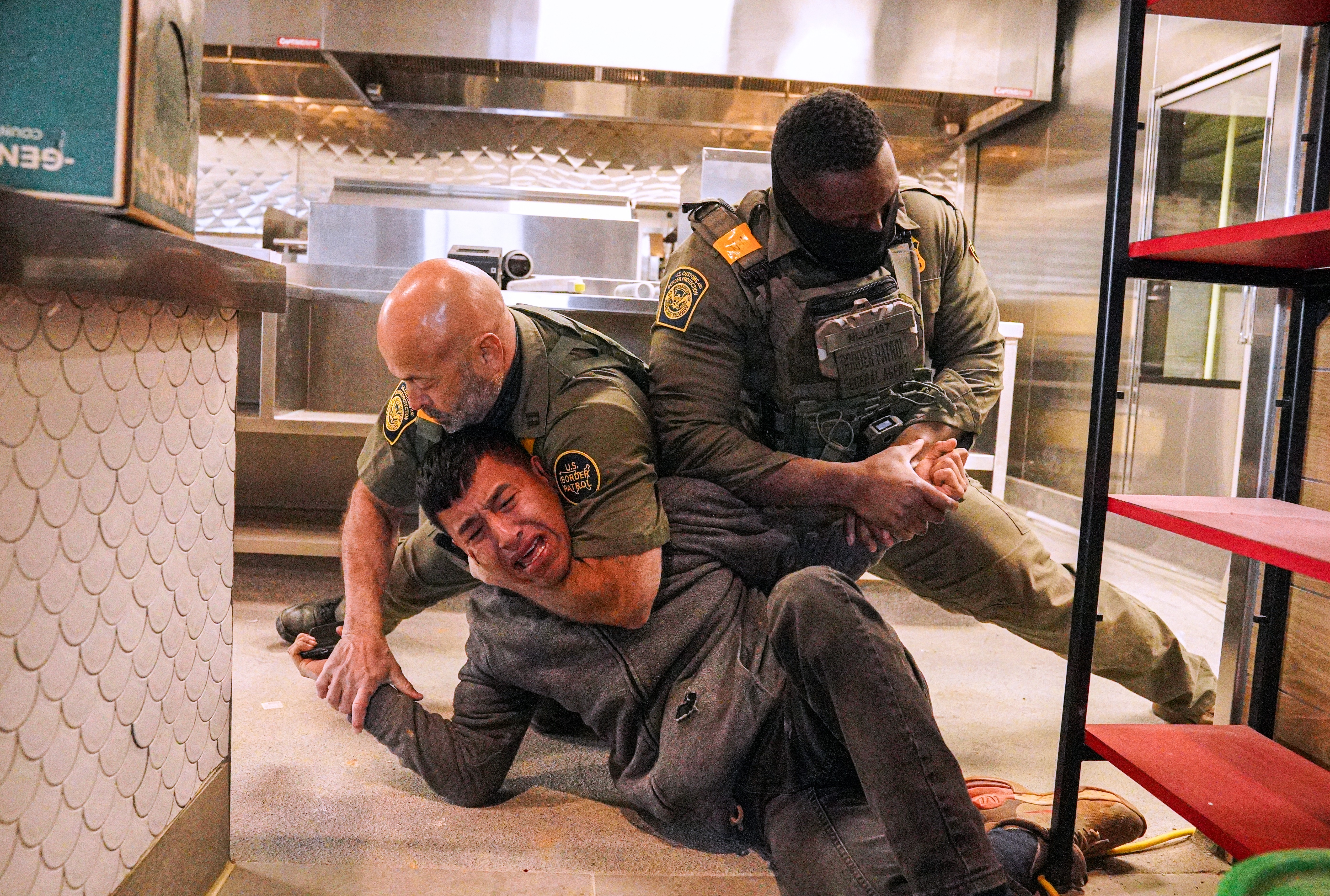 A man grimaces in pain as two U.S. Border Patrol agents wrestle him to the ground inside an under-construction restaurant.