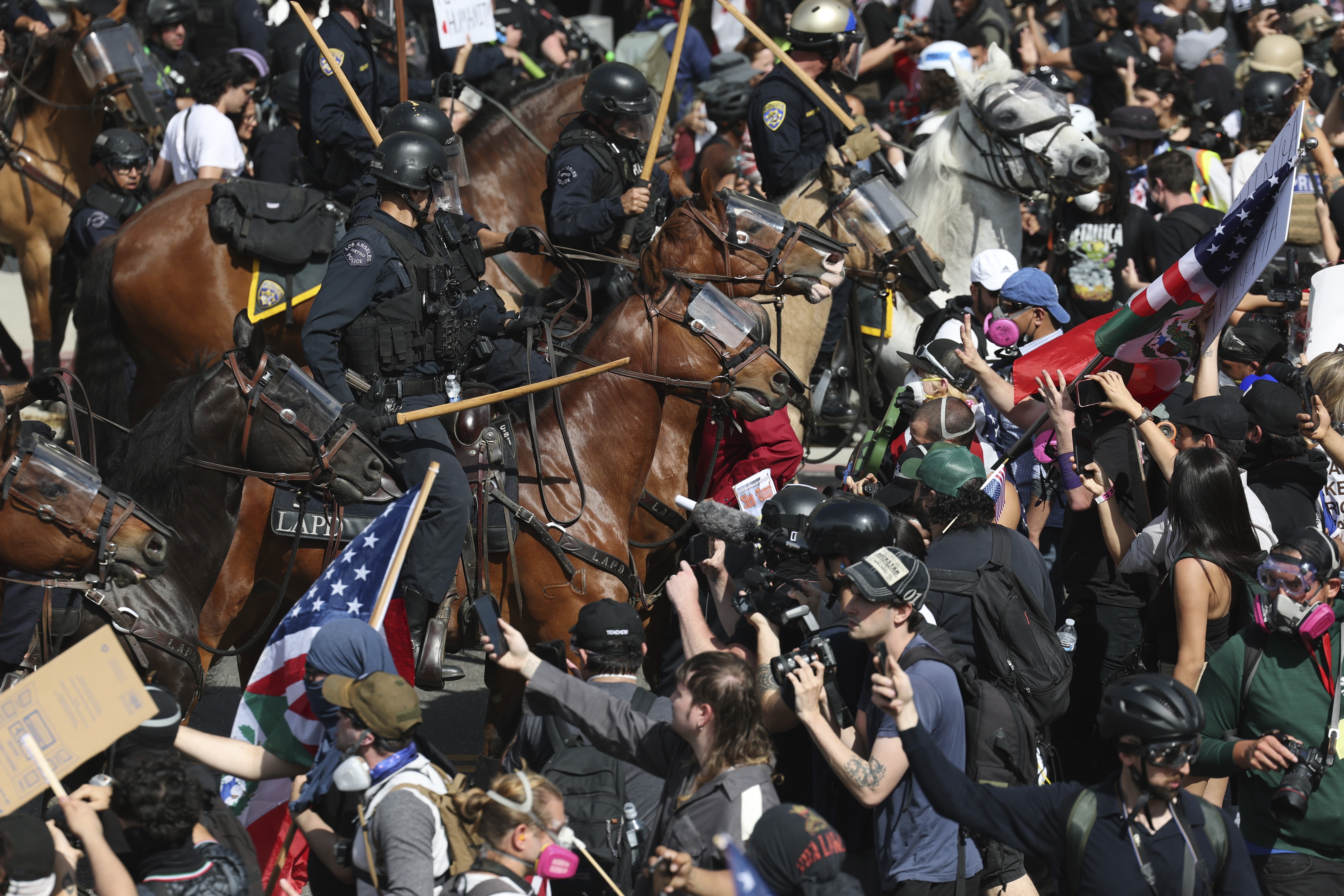 Riot police officers on horseback approach a large crowd of demonstrators.