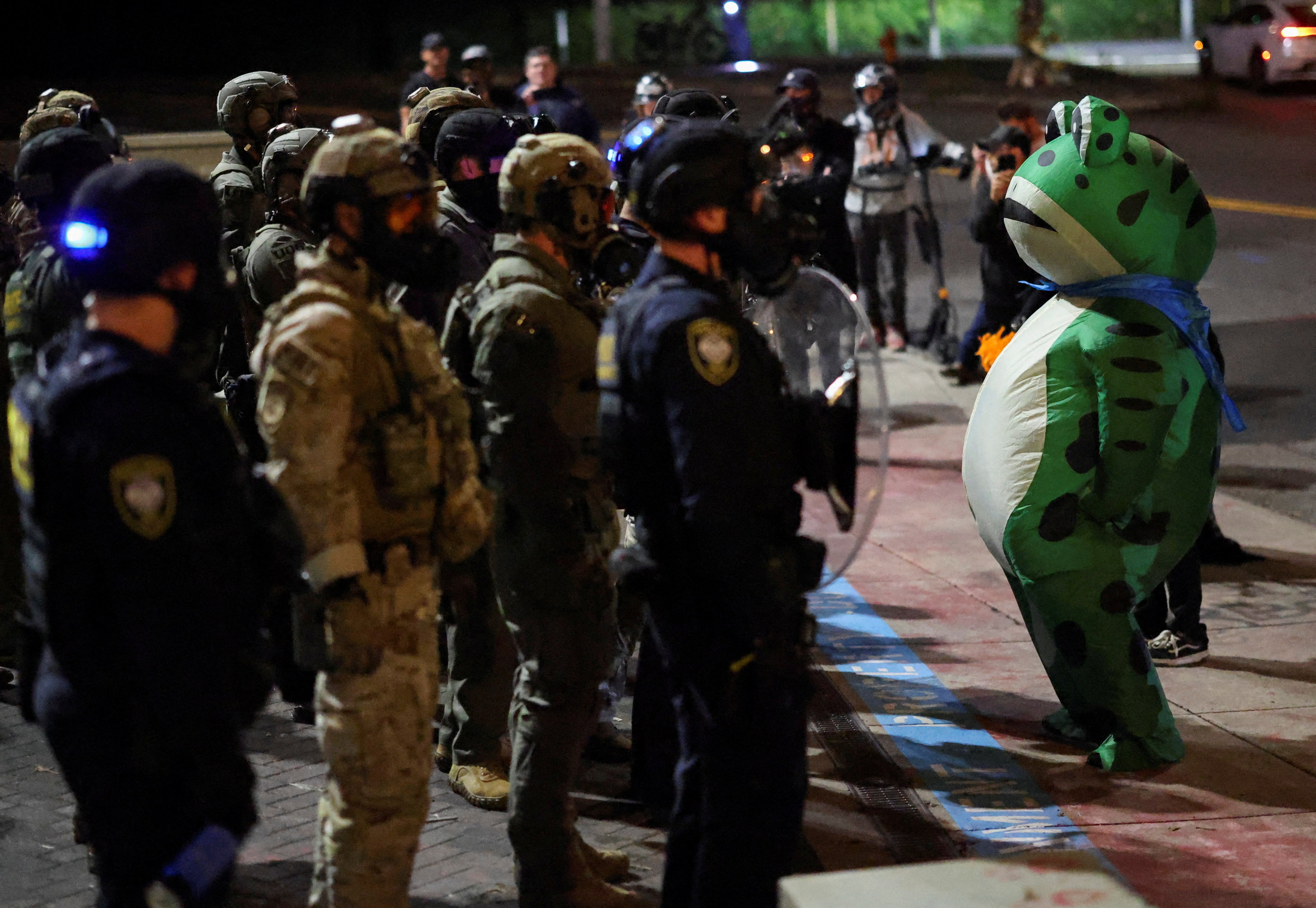 A protester in an inflatable frog costume faces off against several federal law enforcement officers.