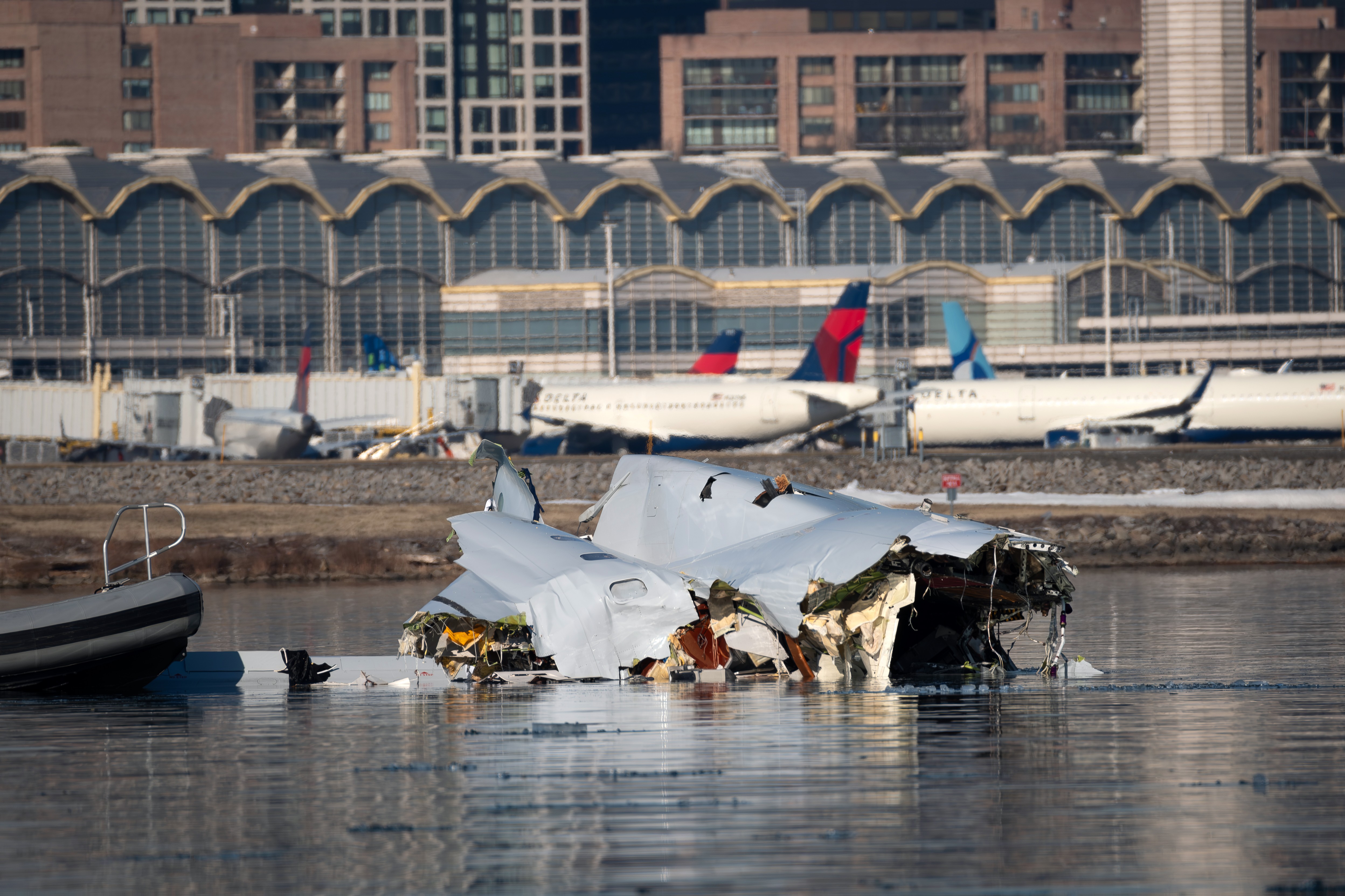 Wreckage from a small passenger aircraft floats in a river, with an airport visible in the background.