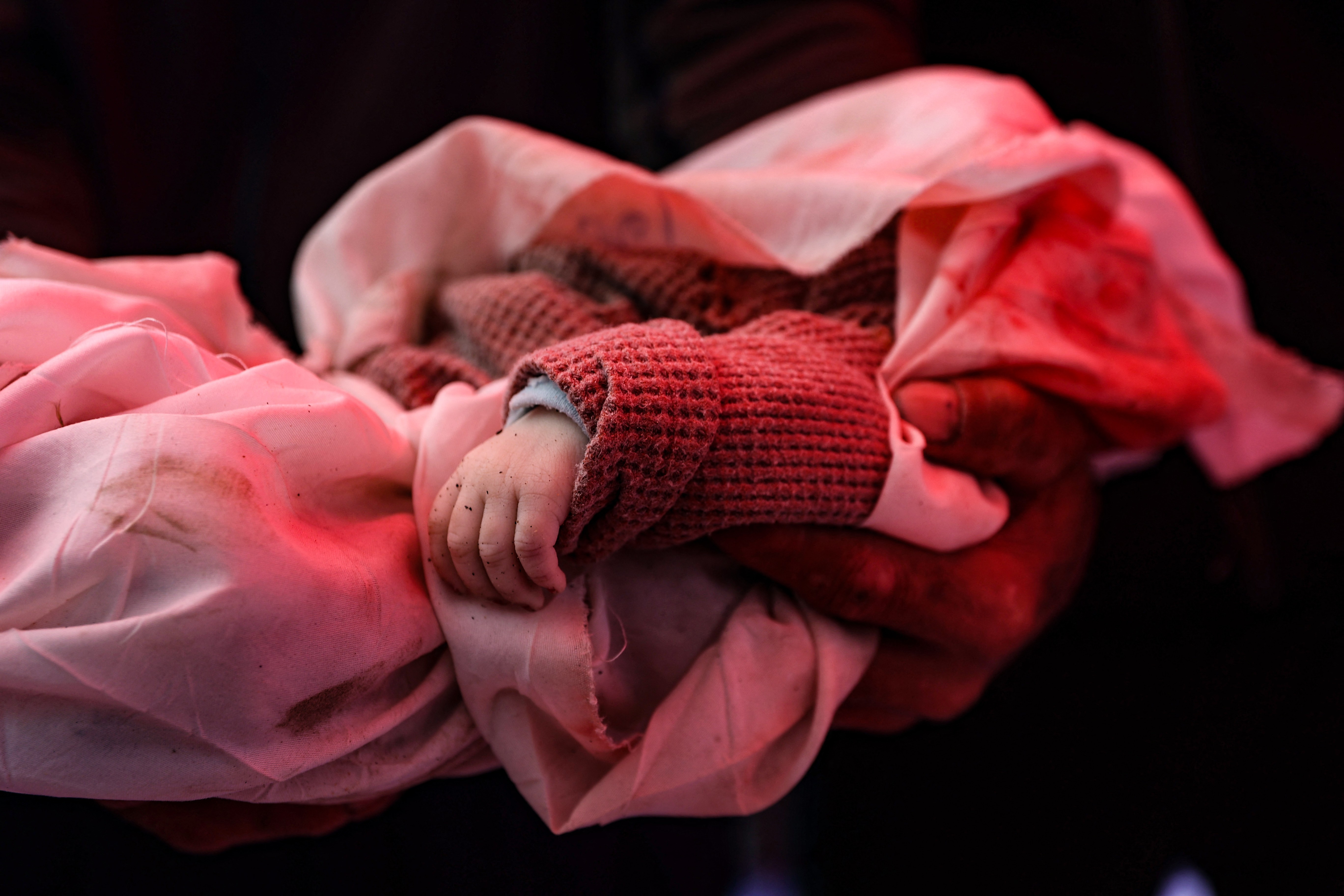 A man carries the body of a child, wrapped in red cloth, who was reportedly killed in an Israeli airstrike.