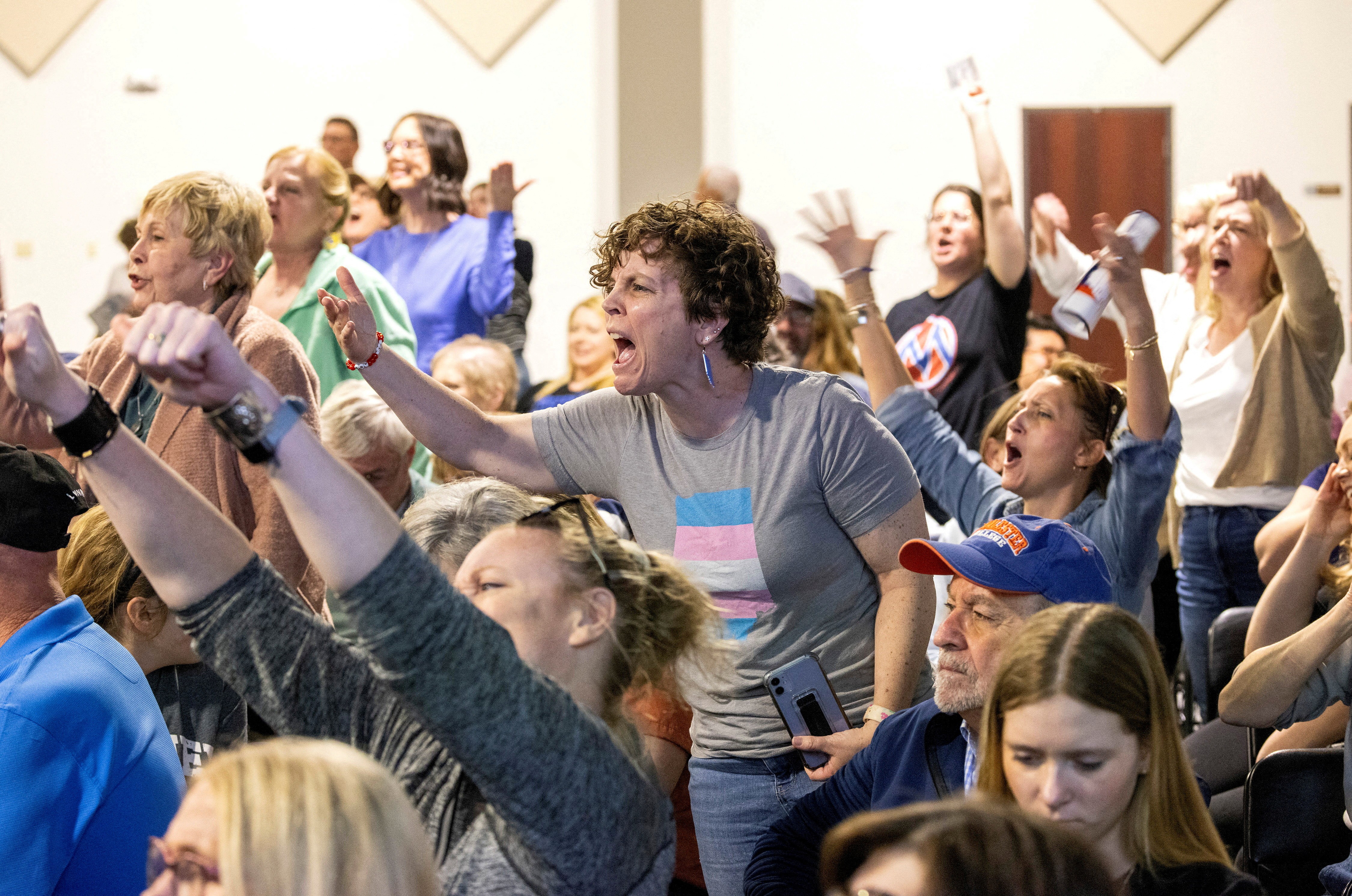 Angry people in a crowd gesture and yell toward a speaker during a town hall.