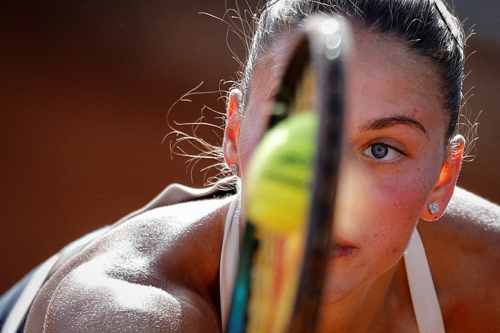 A tennis player hits a tennis ball, which is seen smashed against the face of their racket.