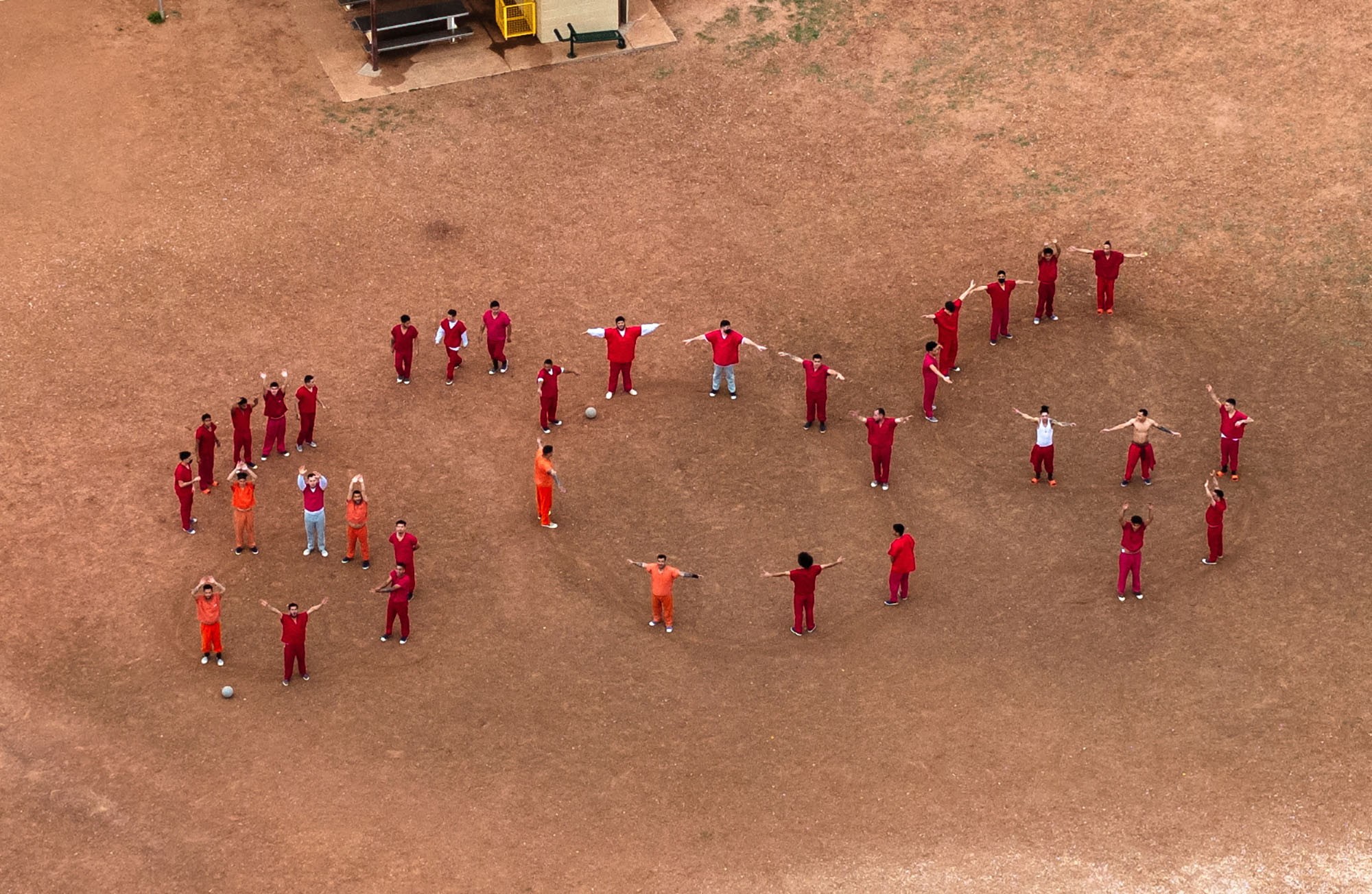 A drone view of detainees forming the letters 'SOS' with their bodies in a prison courtyard