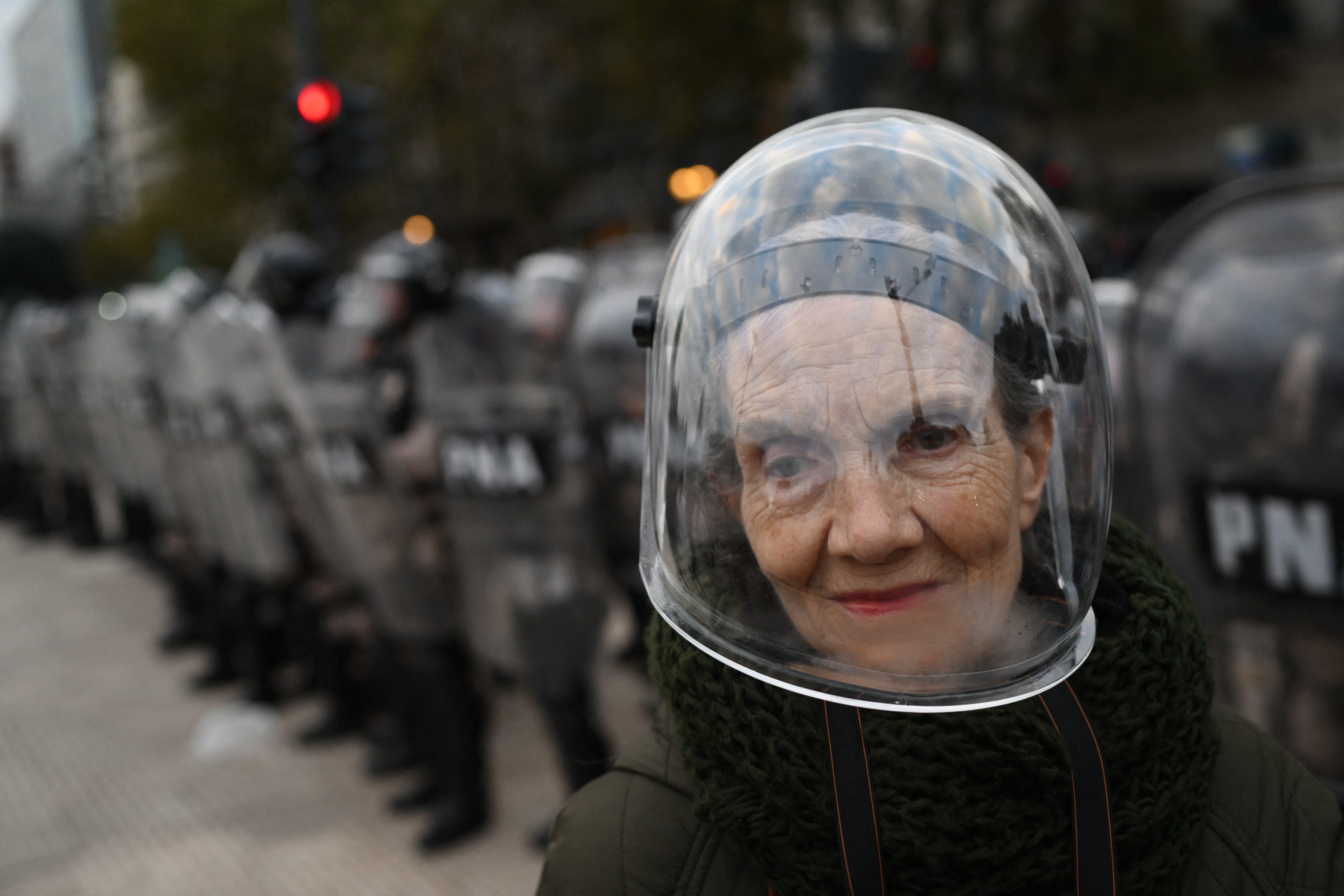 A woman wearing a protective helmet poses in front of a line of riot police during a protest.
