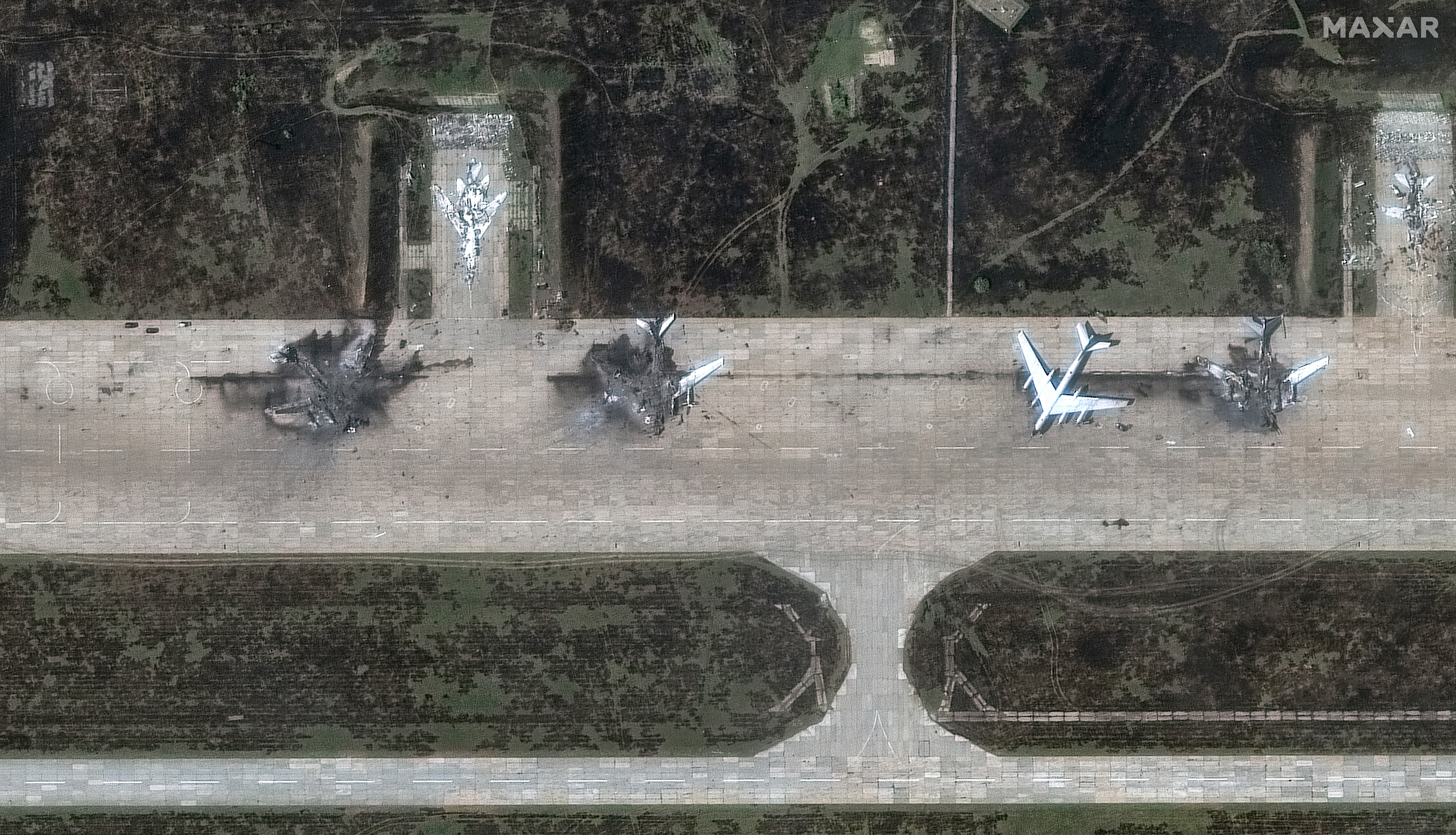 A satellite view of the charred remains of several large bomber aircraft, on an airfield