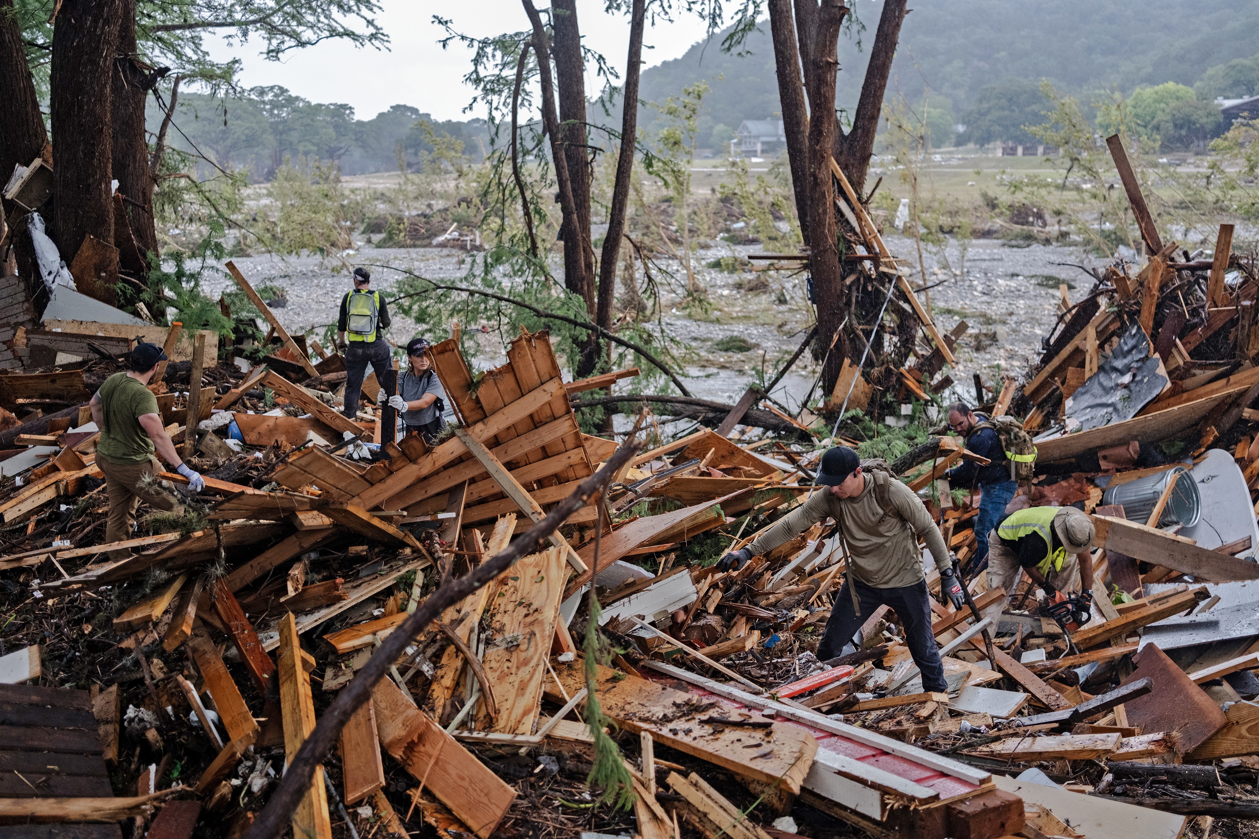 Search and rescue workers dig through debris alongside a recently-flooded riverbed.