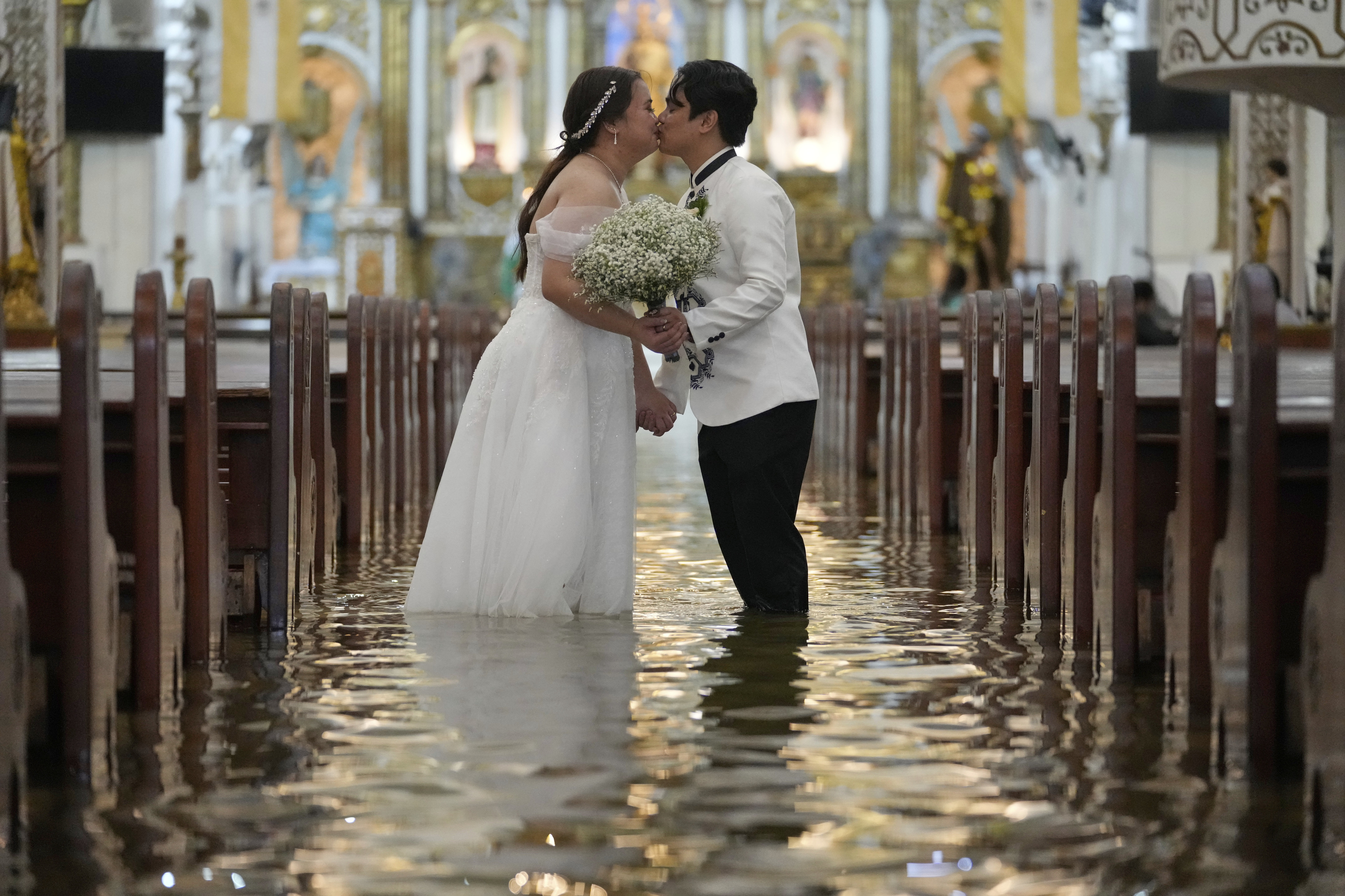 A newlywed couple kisses after a wedding ceremony inside a church that has been flooded, with about a foot of standing floodwater.