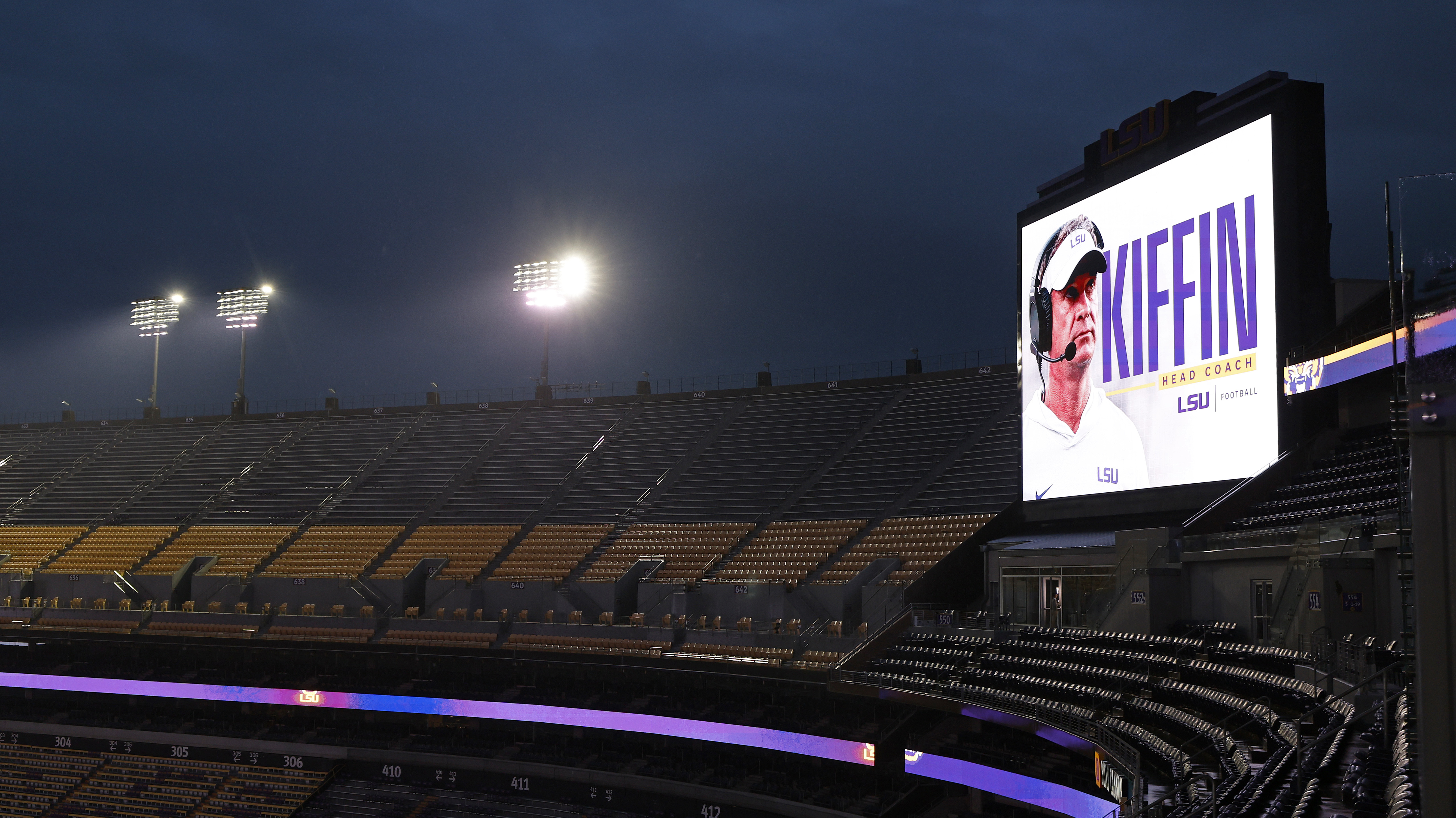 Photograph of an empty stadium at night with a giant screen showing Lane Kiffin's name and photo as head coach of Louisiana State University