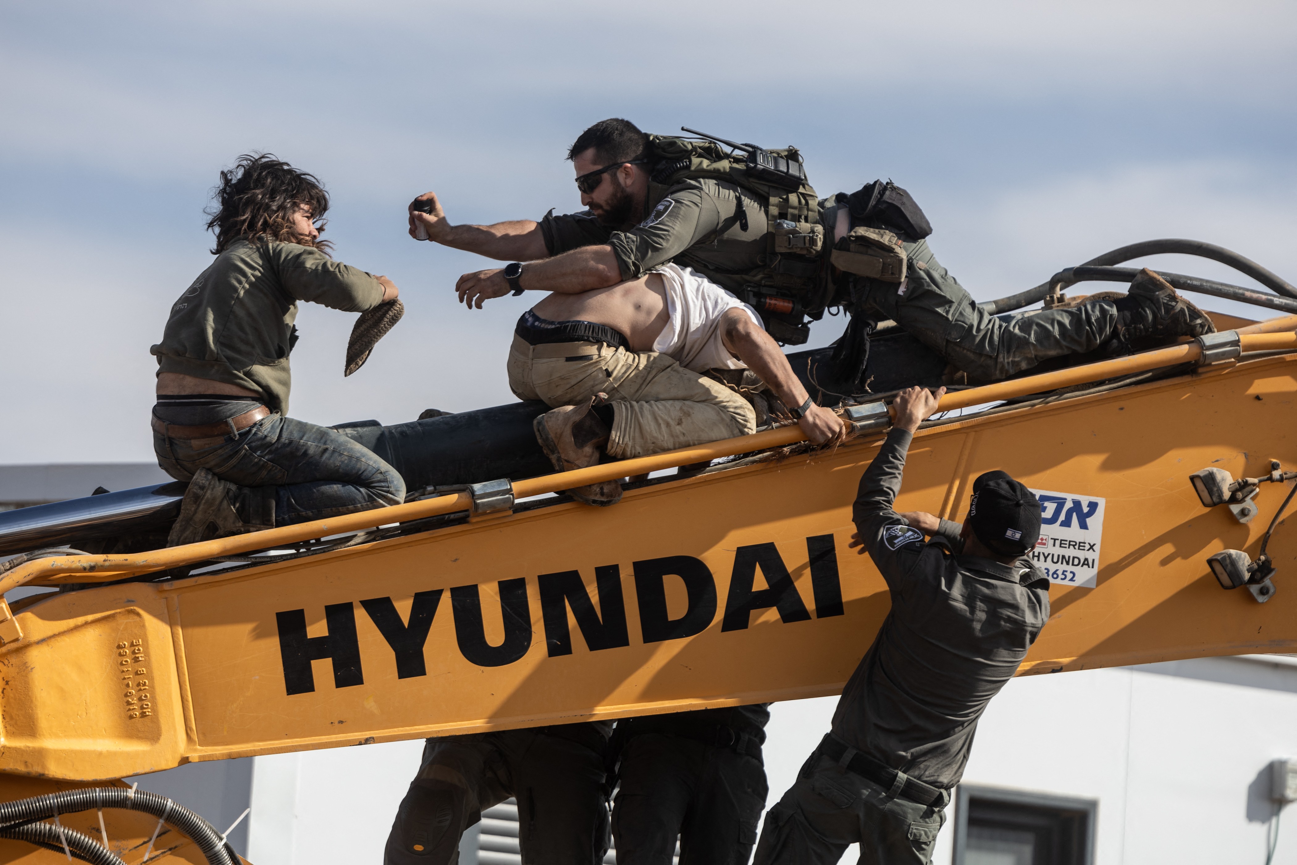 Several soldiers struggle with civilians atop the long arm of a piece of construction equipment.