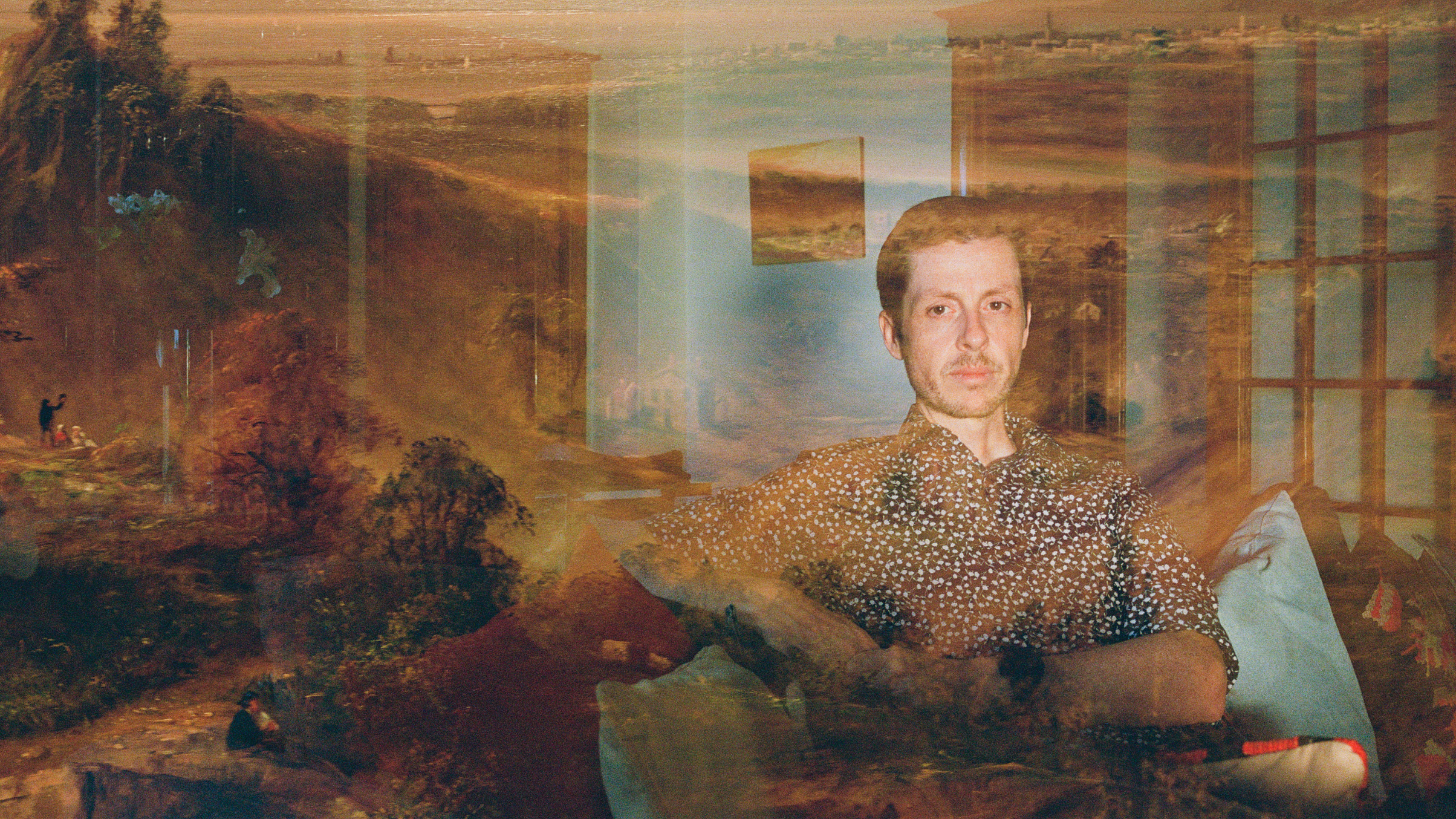 photo with a double exposure, one of a man sitting in his living room next to a guitar with a hazy overlay of a 17th-century landscape painting