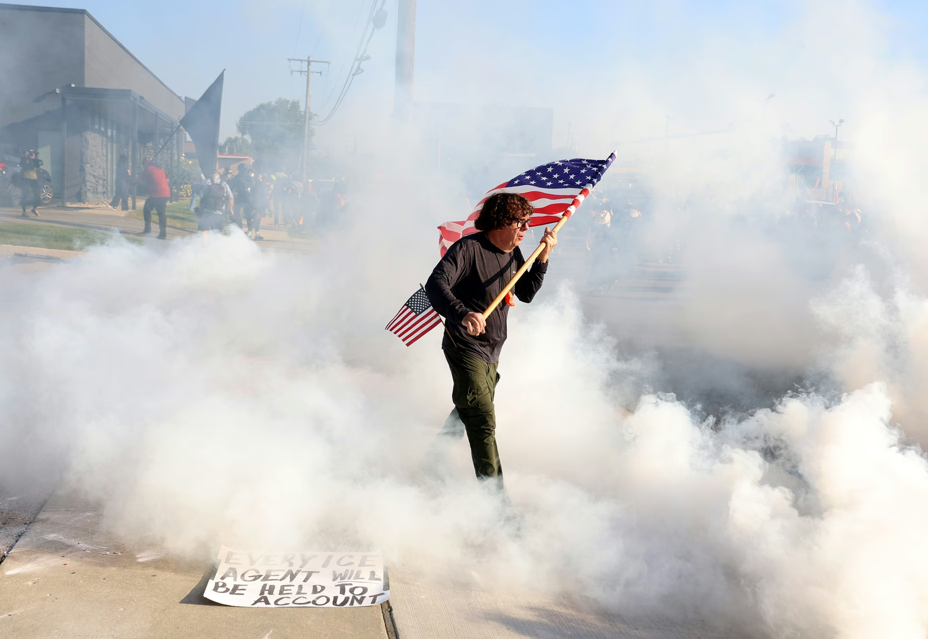 A man carries an American flag through gas that was deployed by federal officers as they cleared protesters from the entrance of the ICE facility in Broadview, Illinois.