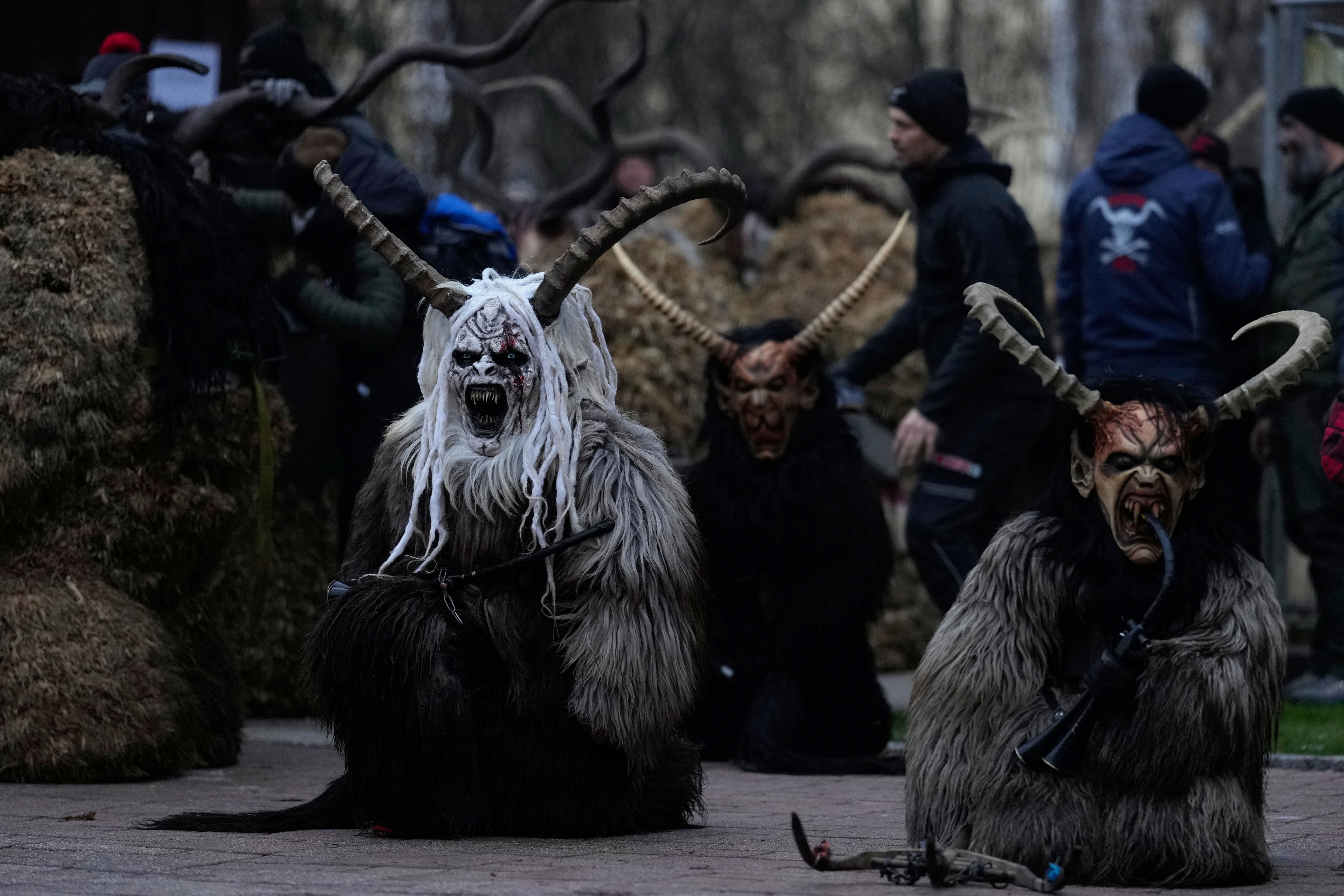 People wearing scary, horned, demon costumes gather on a street.