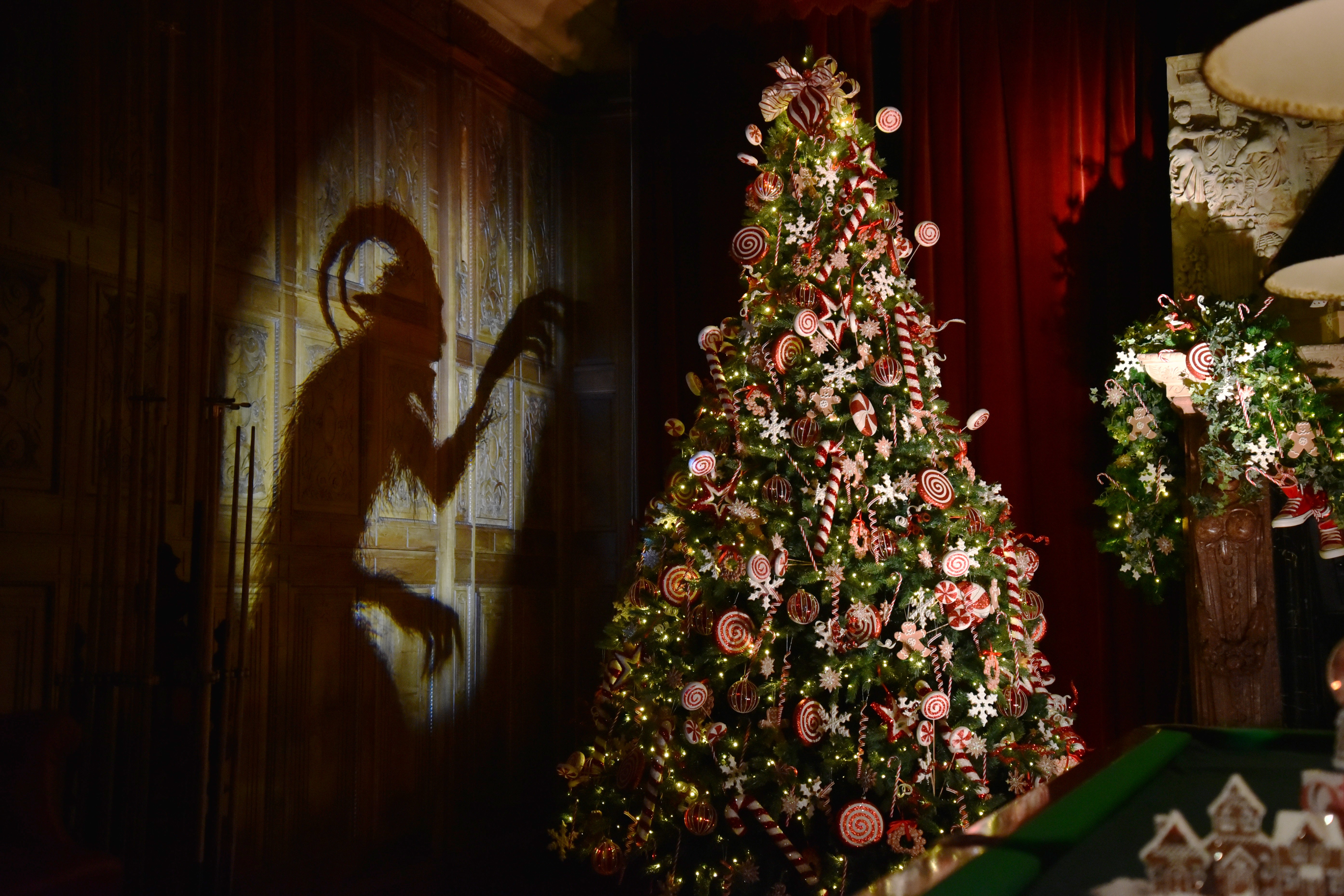 A Christmas display inside a large manor, including a decorated Christmas tree and the shadowy outline of a Krampus figure projected against a wall