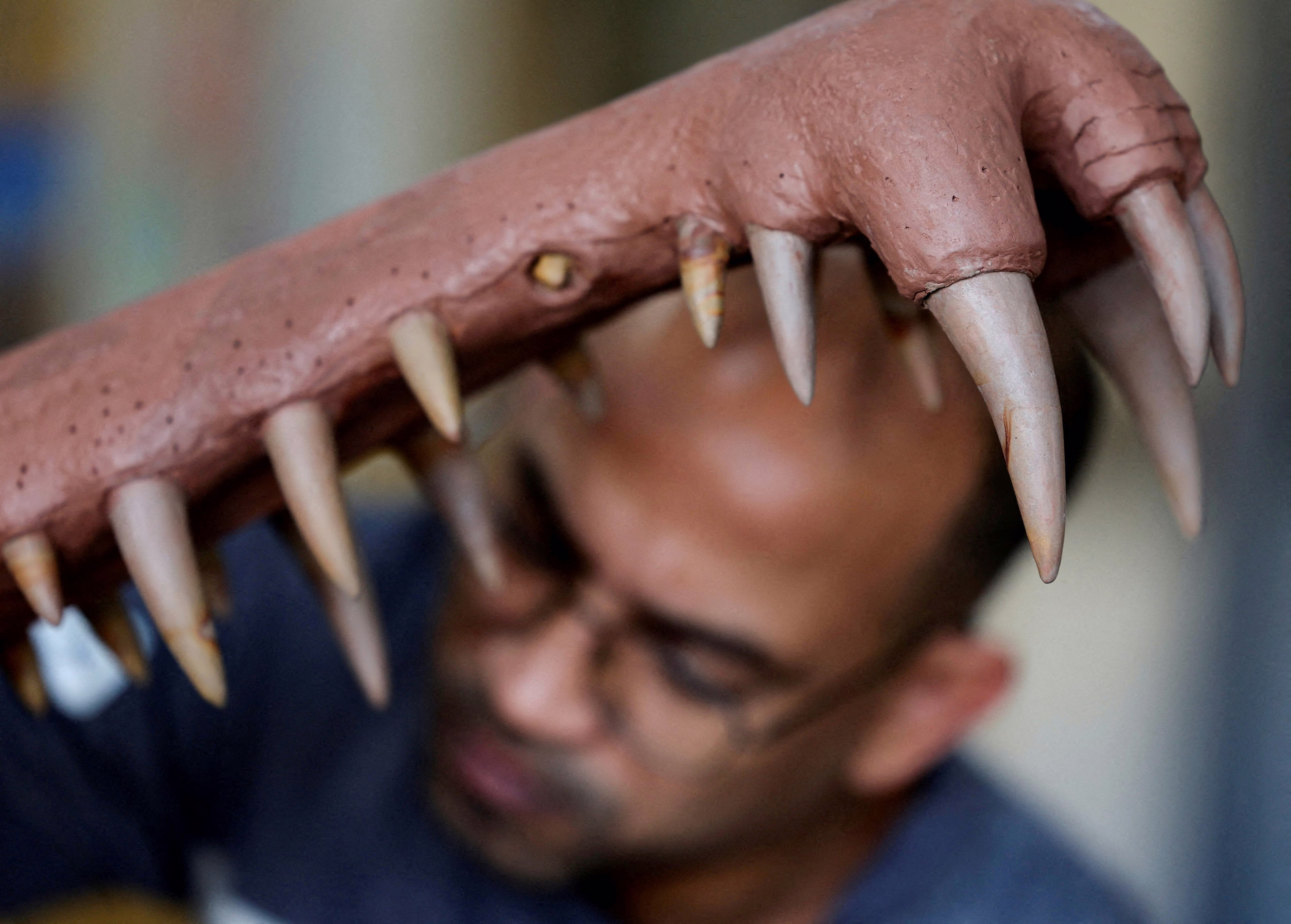 A person works beside the open jaw of a sculpture of a prehistoric crocodile.