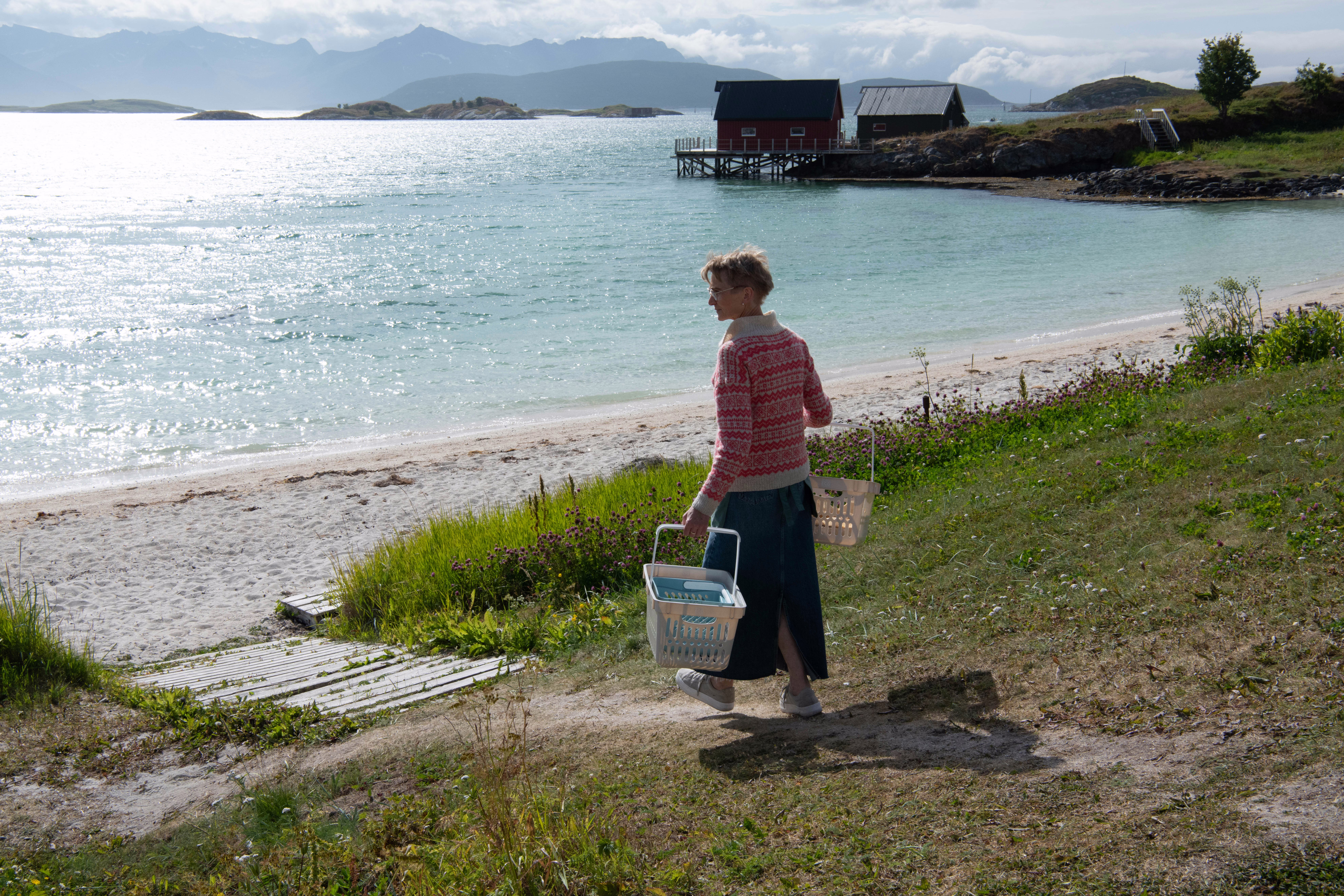 A color photograph of a woman carrying large baskets while walking to the beach