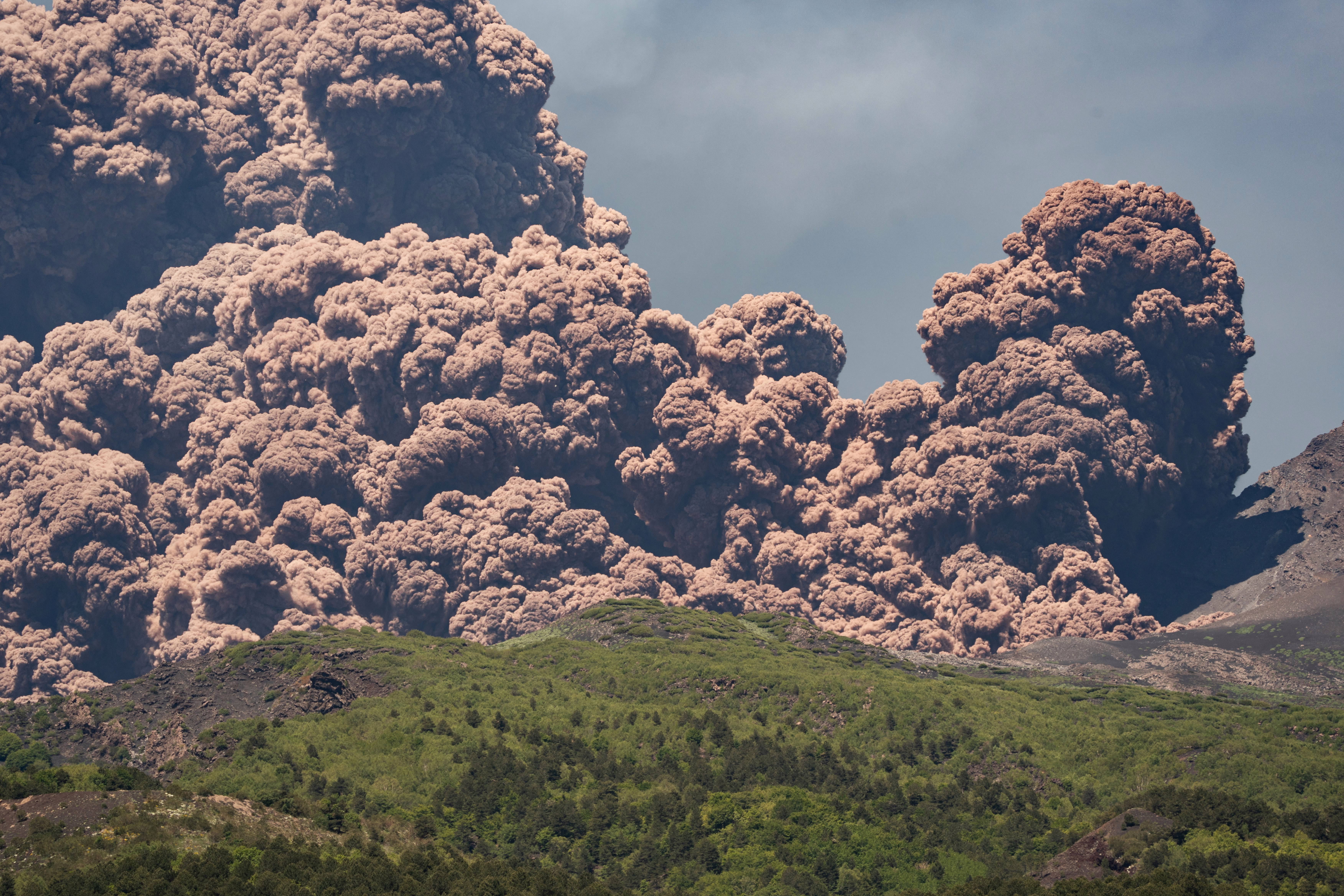 A large plume of brownish-colored ash rises from the top of a volcano.